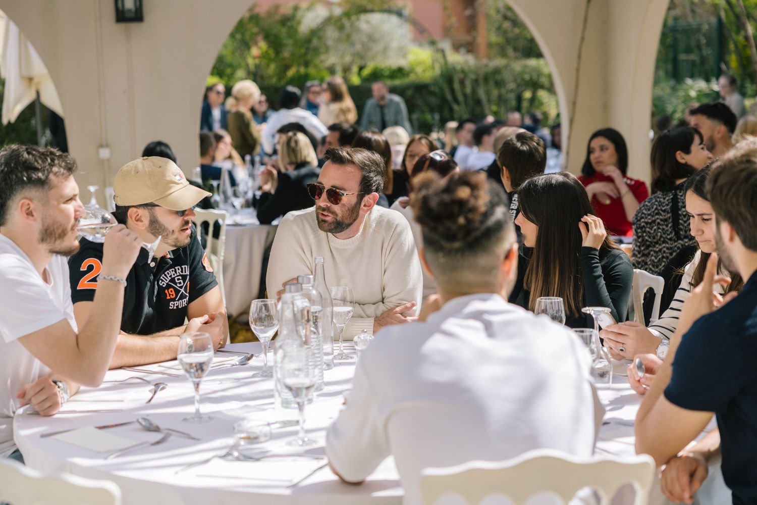 Group of people enjoying conversation around an outdoor dining table at a restaurant.