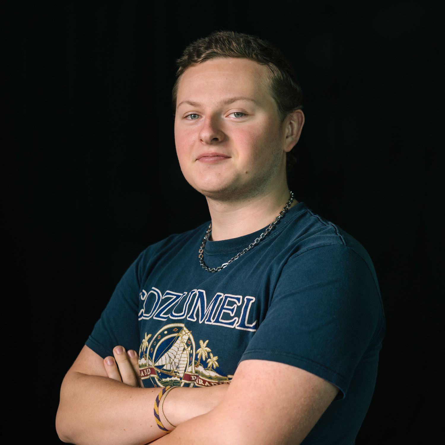 Professional headshot of someone wearing a blue t-shirt against a dark background.