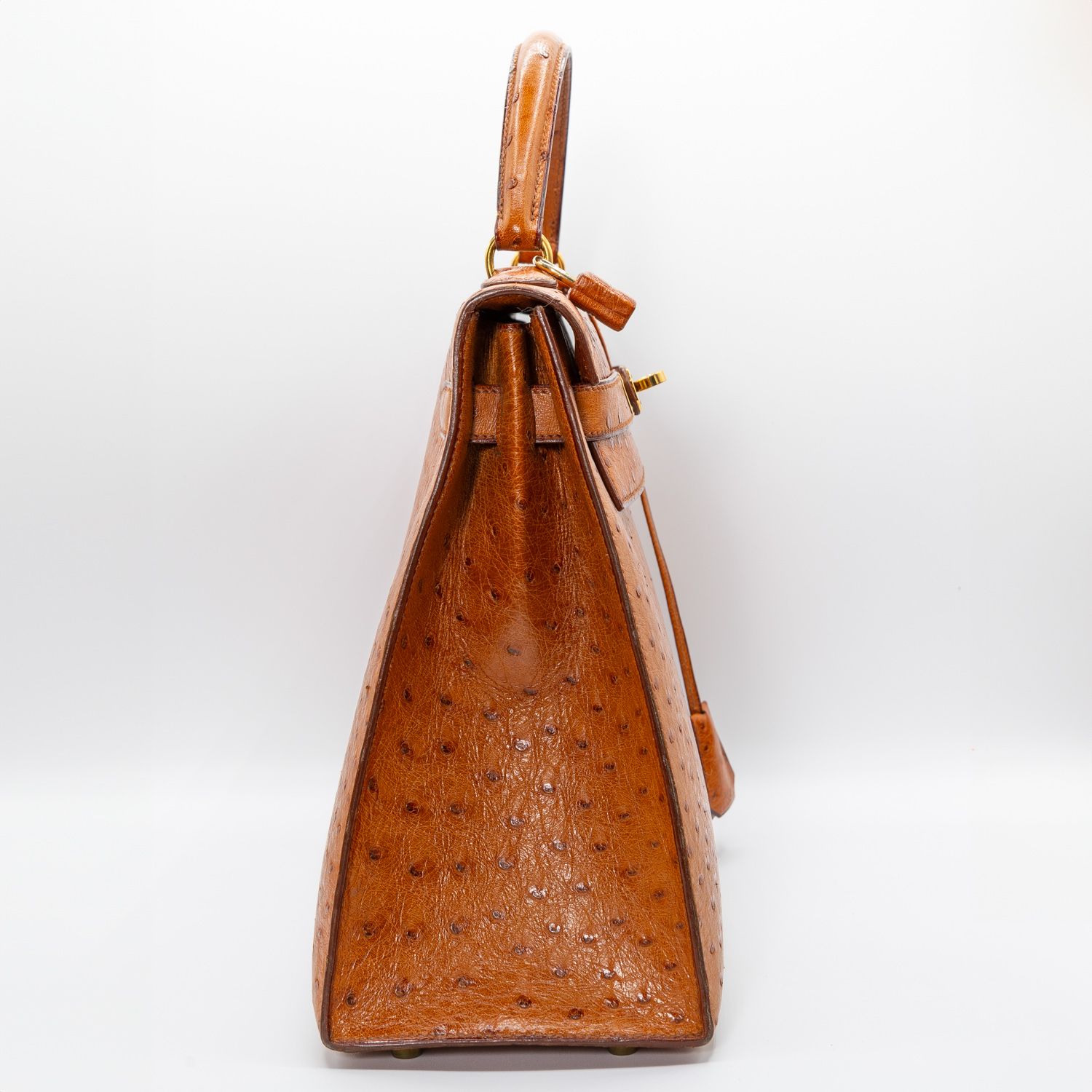 Side view of a tan ostrich leather luxury handbag on white background.
