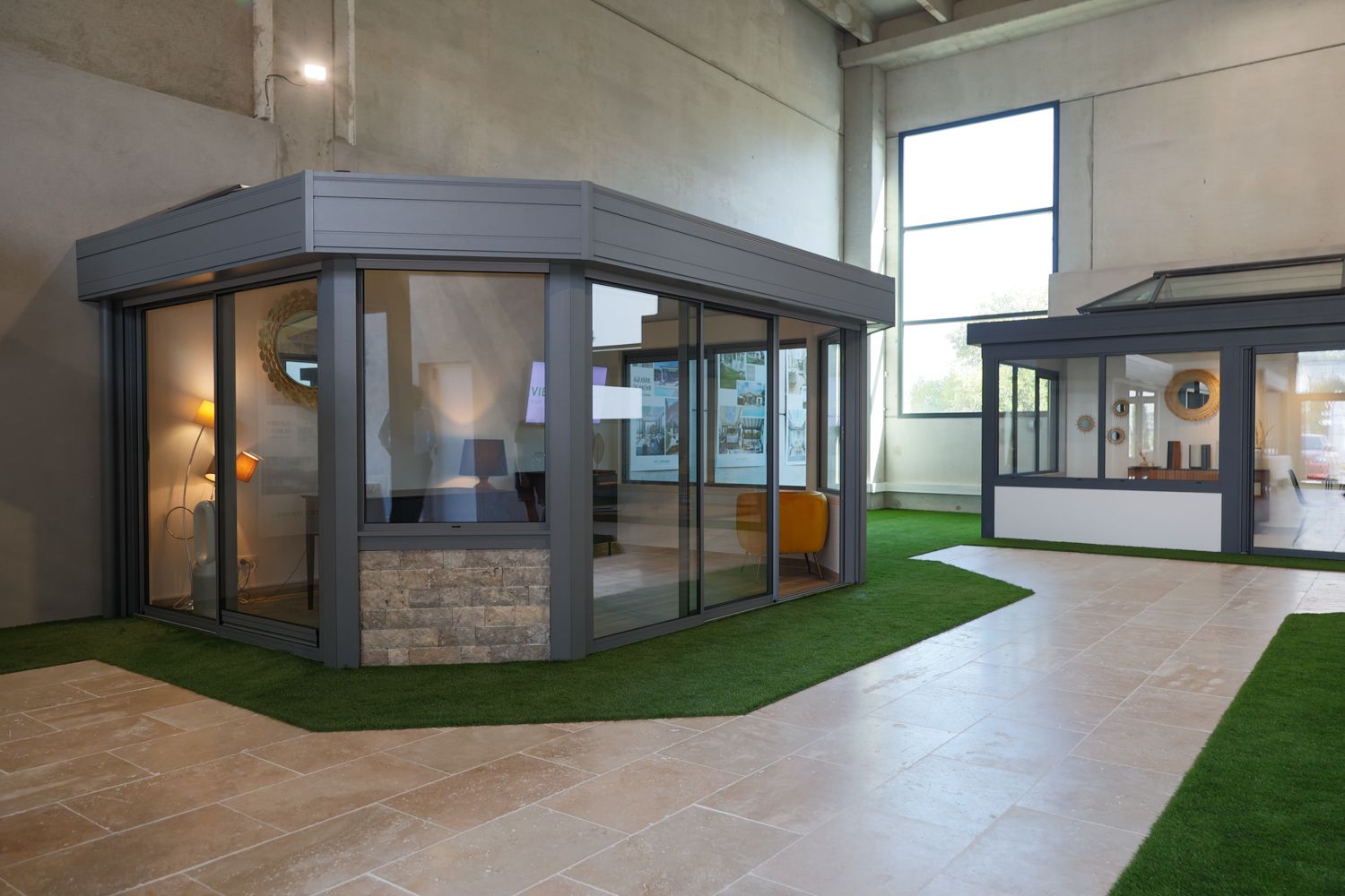 Sleek glass-enclosed display pavilion with stone accents and artificial grass in showroom environment.