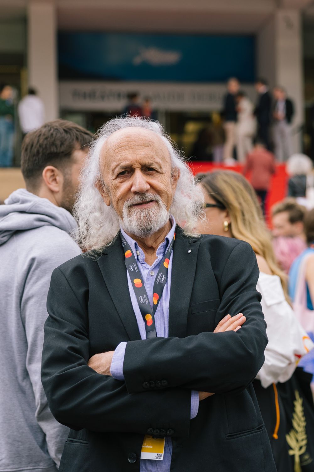 Festival attendee with distinctive white beard and dark jacket stands with crossed arms.