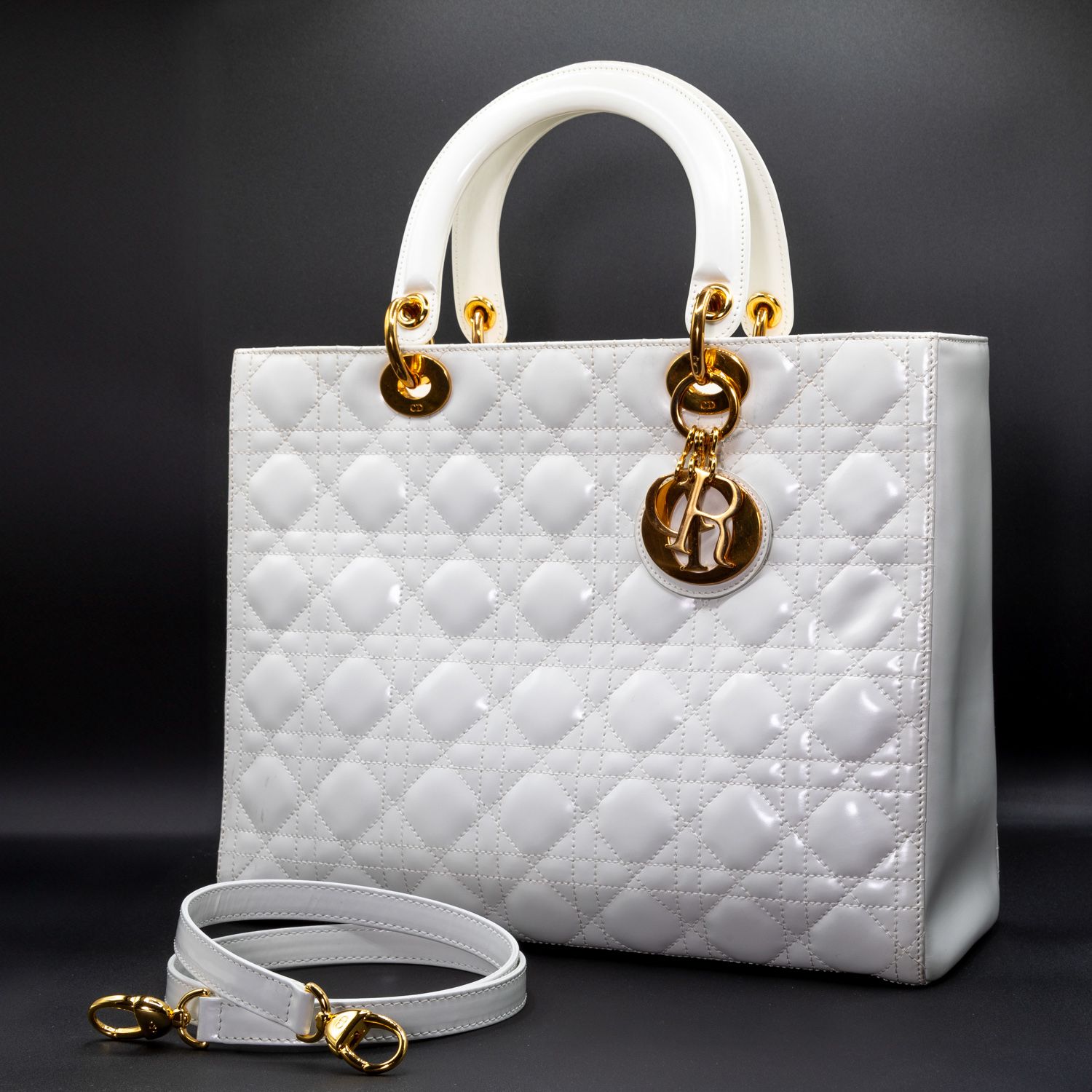 Classic white quilted Lady Dior bag with top handle and shoulder strap on black background.