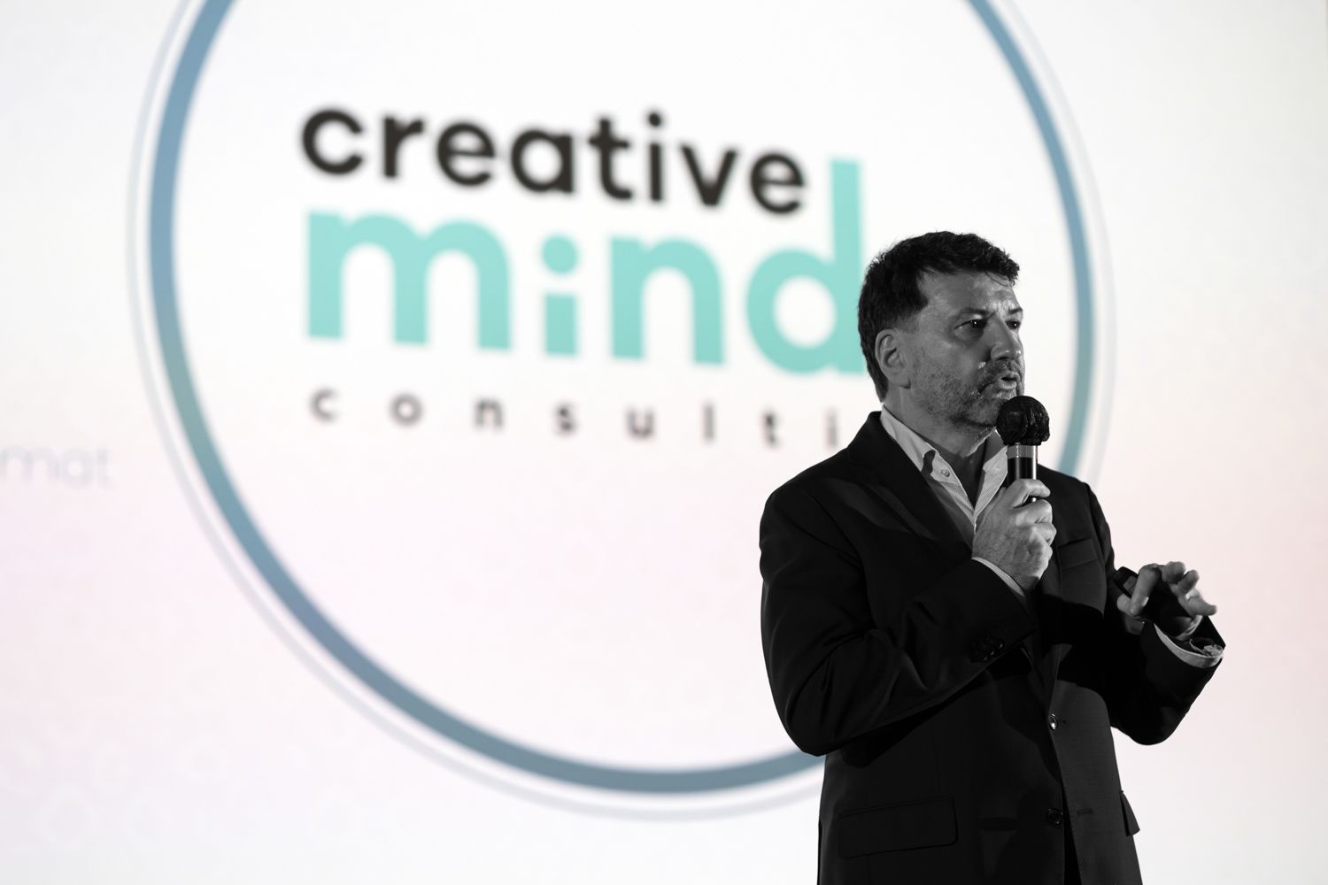 Speaker presenting in front of Creative Mind Consult logo projection in dark room.