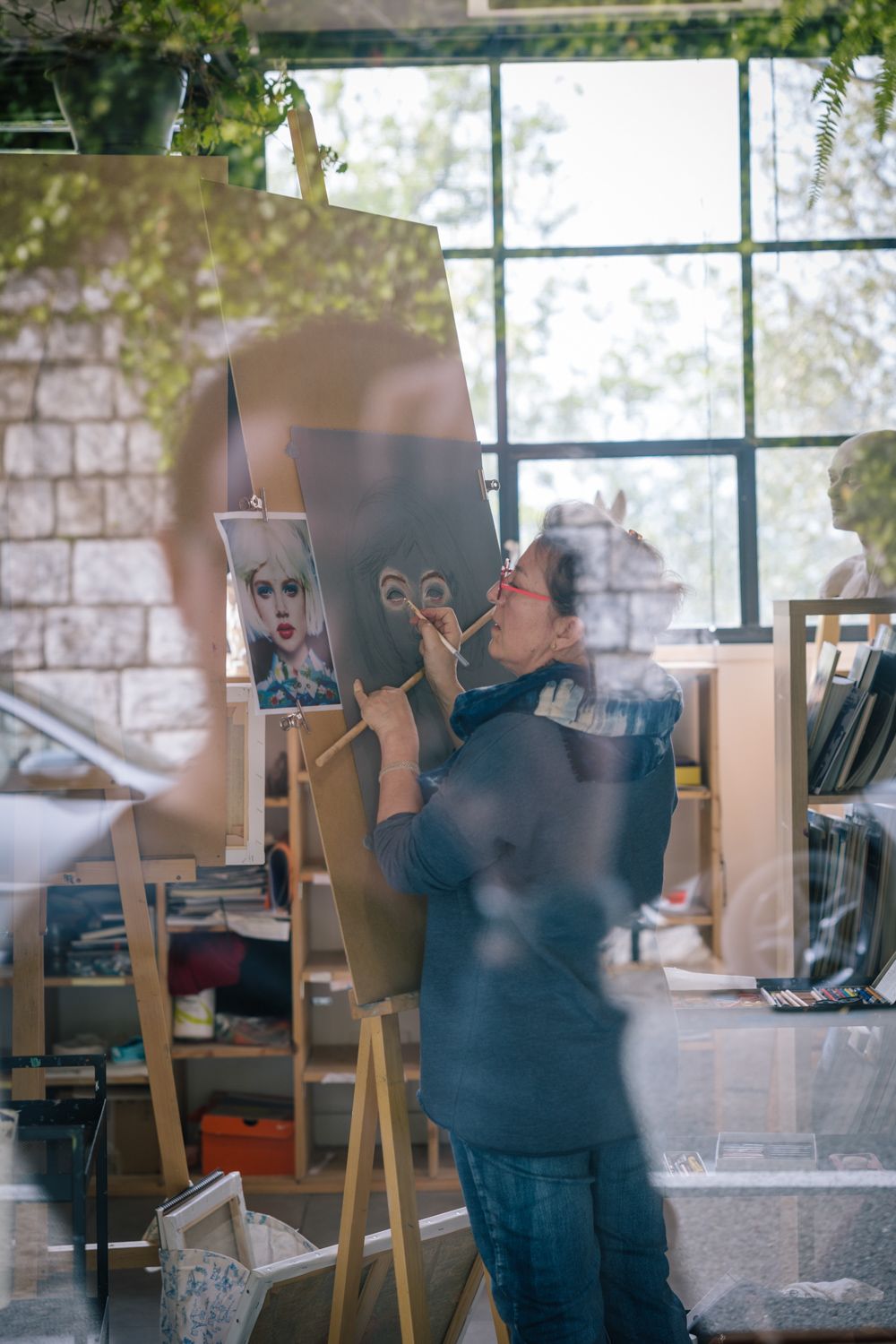Artist working at an easel in a sunlit studio space.