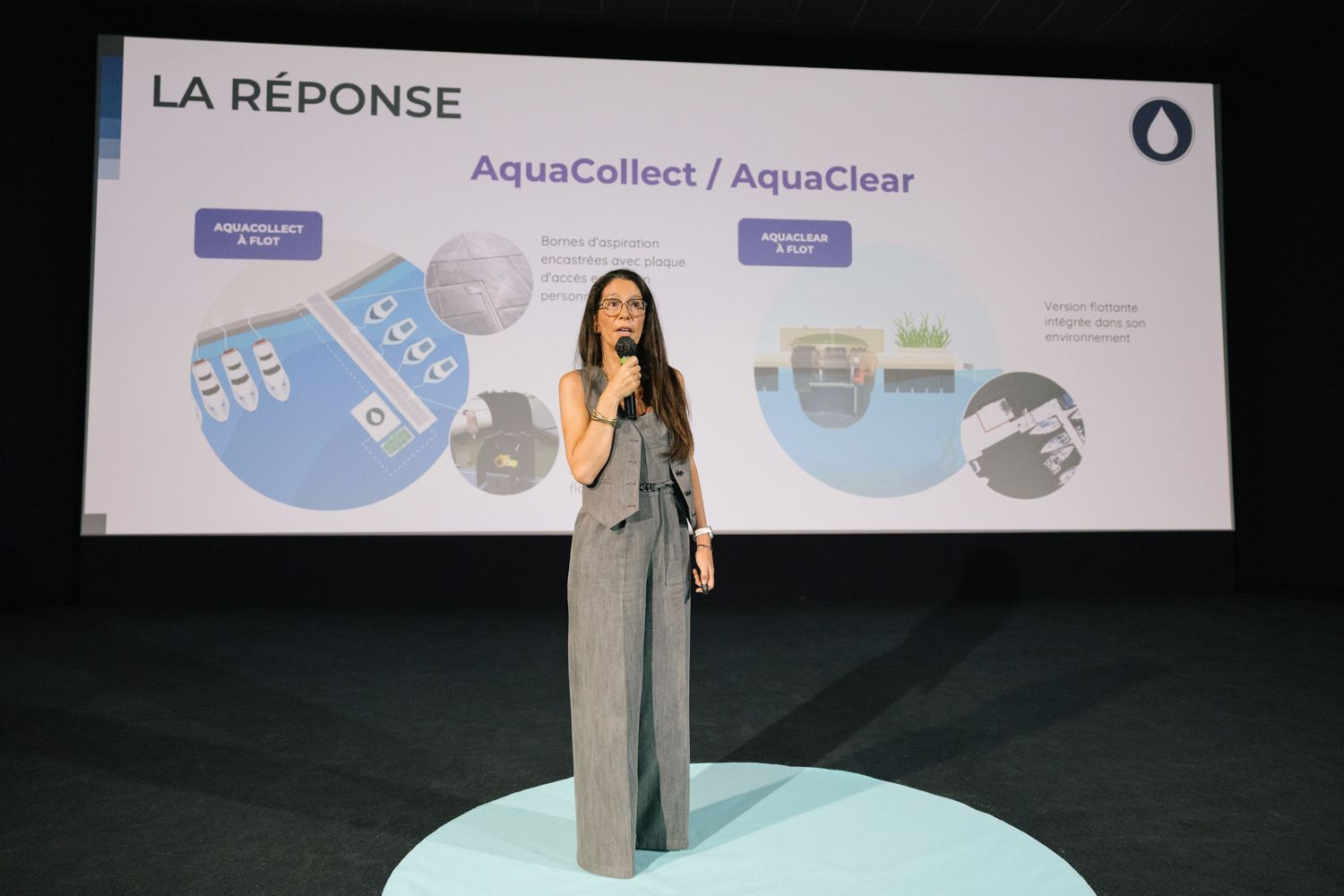 A presenter gives a presentation in front of a large screen displaying AquaCollect and AquaClear logos.