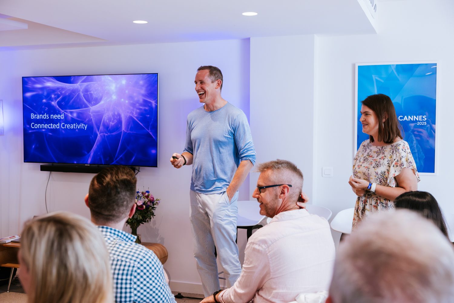 A group of people gather in a modern office space for a business meeting with multiple screens displaying information.