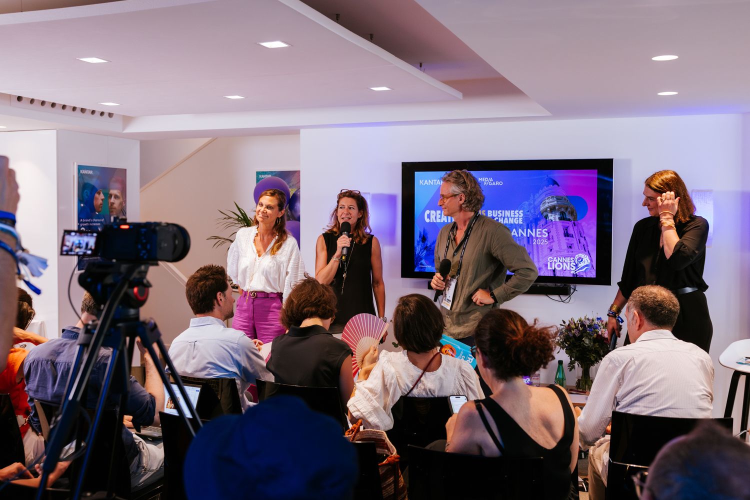 Business professionals networking and mingling at a corporate event with TV screens and presentation displays.