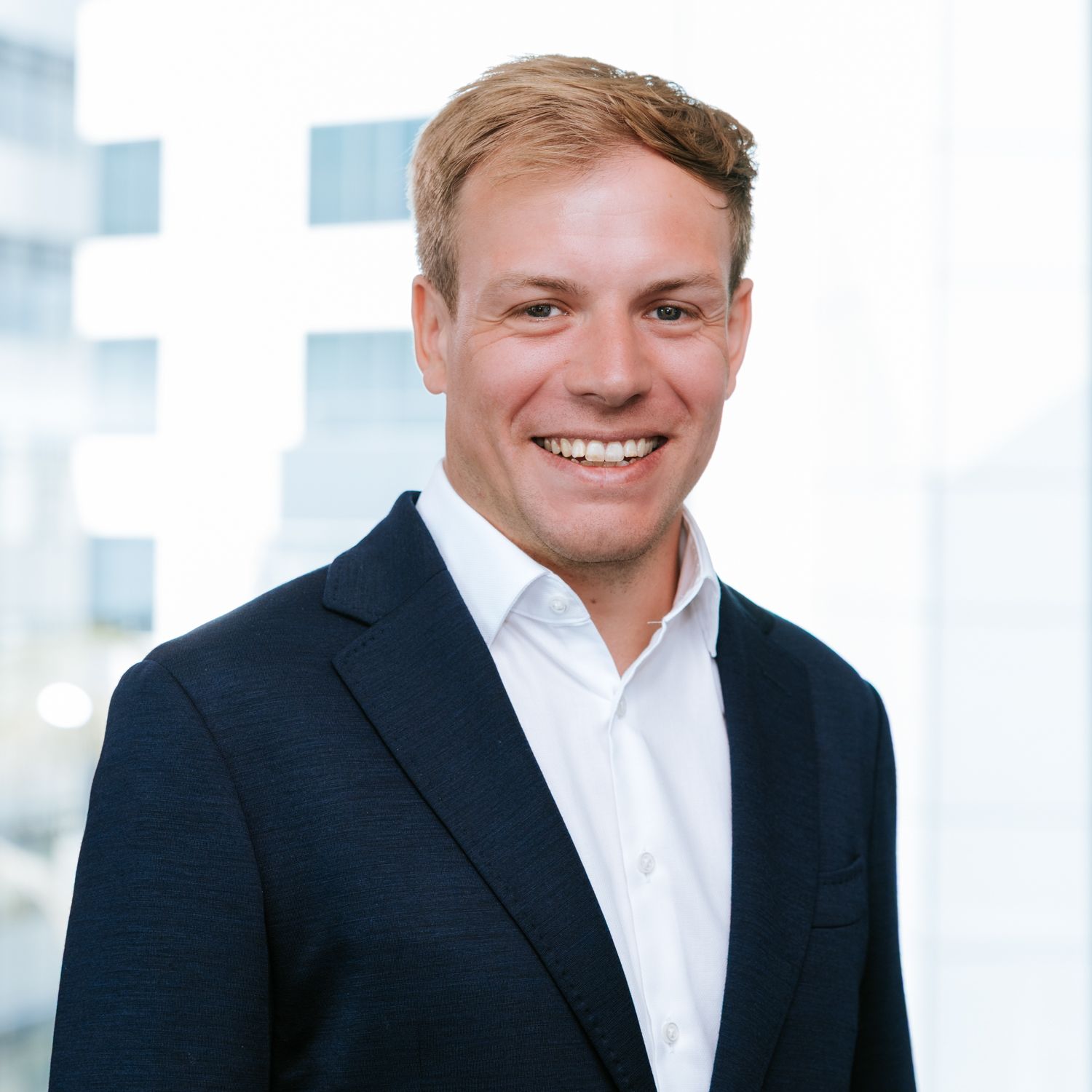 Professional headshot of a person in a dark suit and white shirt against a light background.