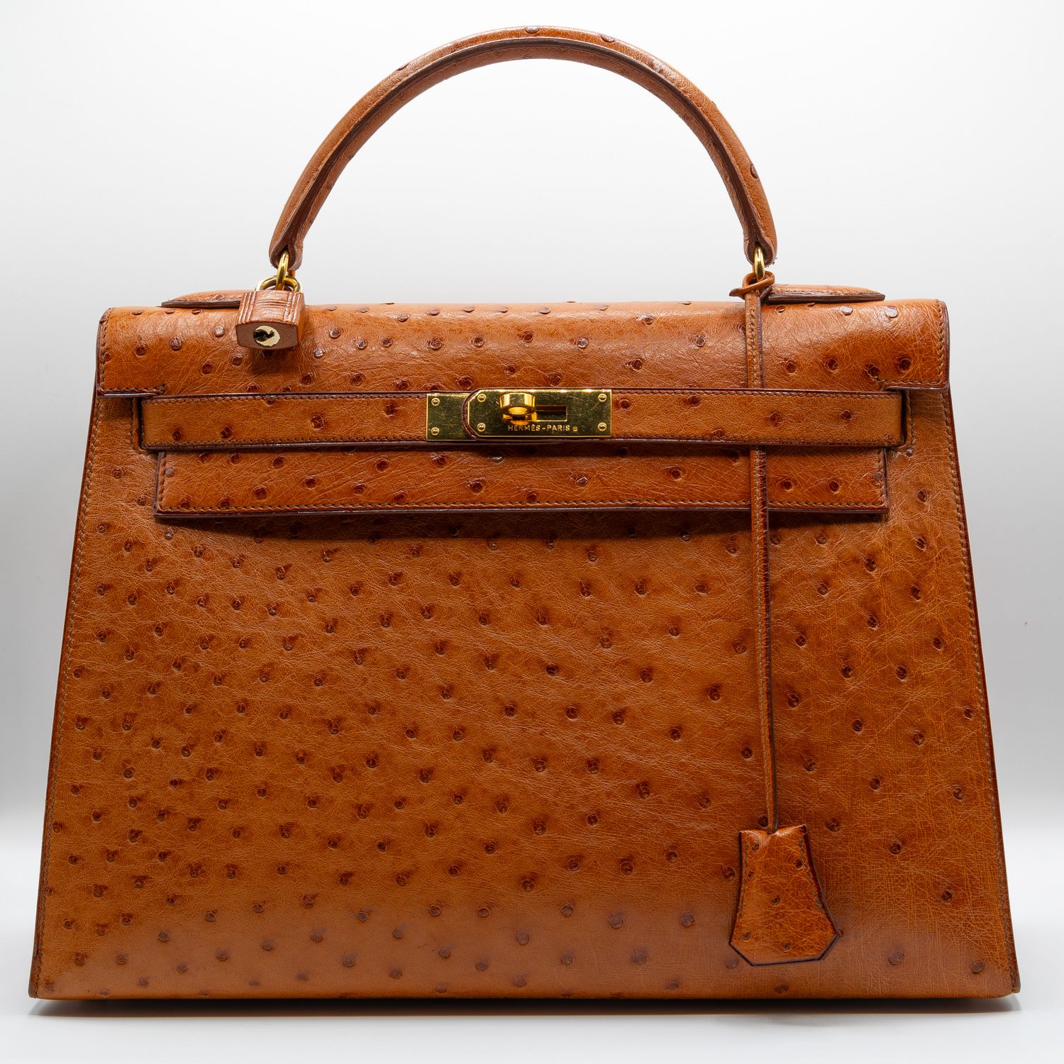 Front view of a cognac-colored ostrich leather designer handbag with gold hardware.