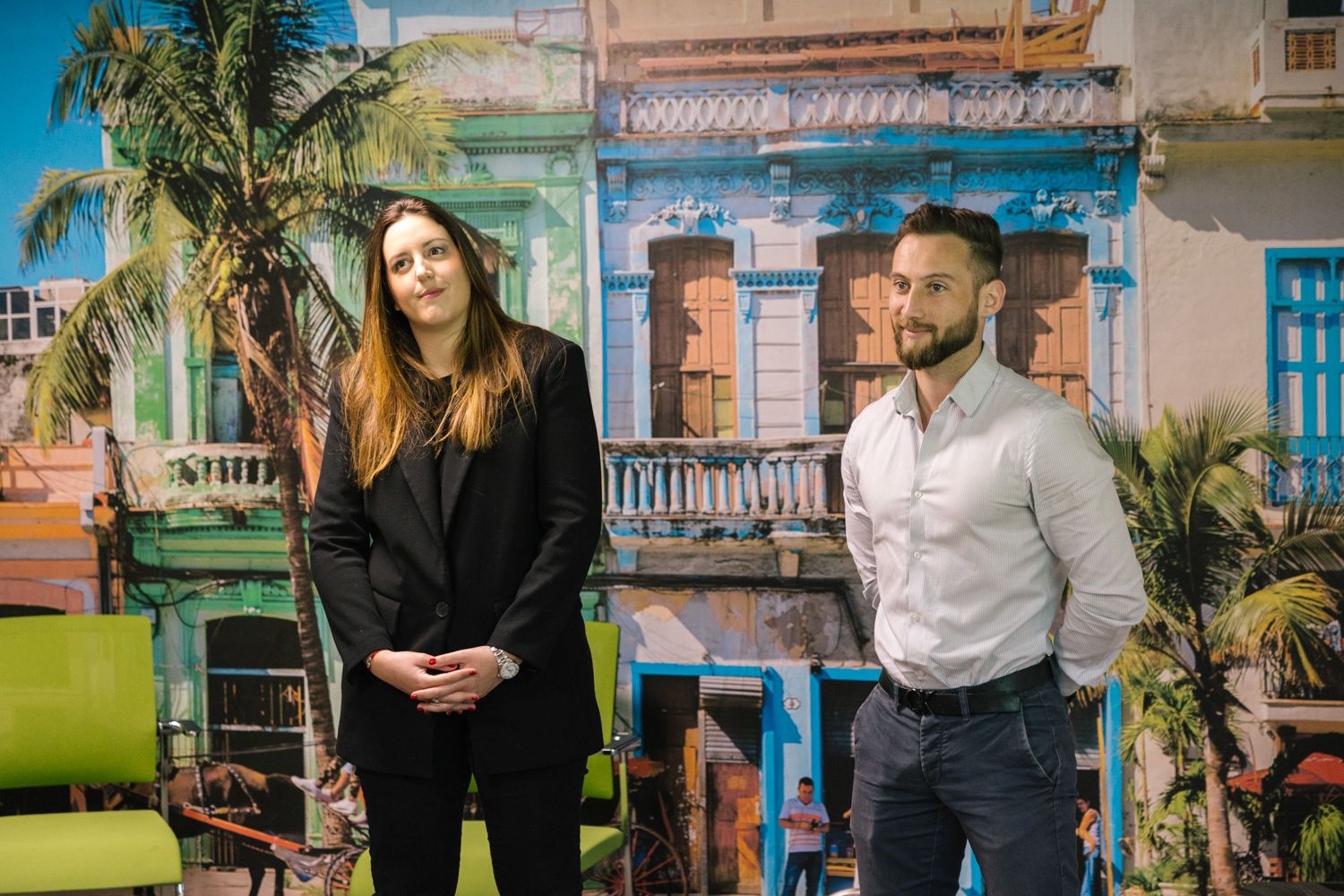 Two professionals standing in front of a colorful tropical backdrop during a presentation.