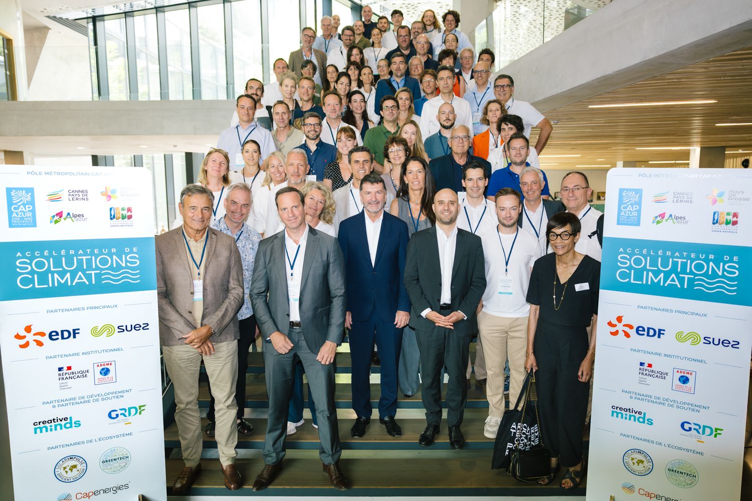 Large group of business professionals gathered in an office lobby with corporate banners and signage displayed.