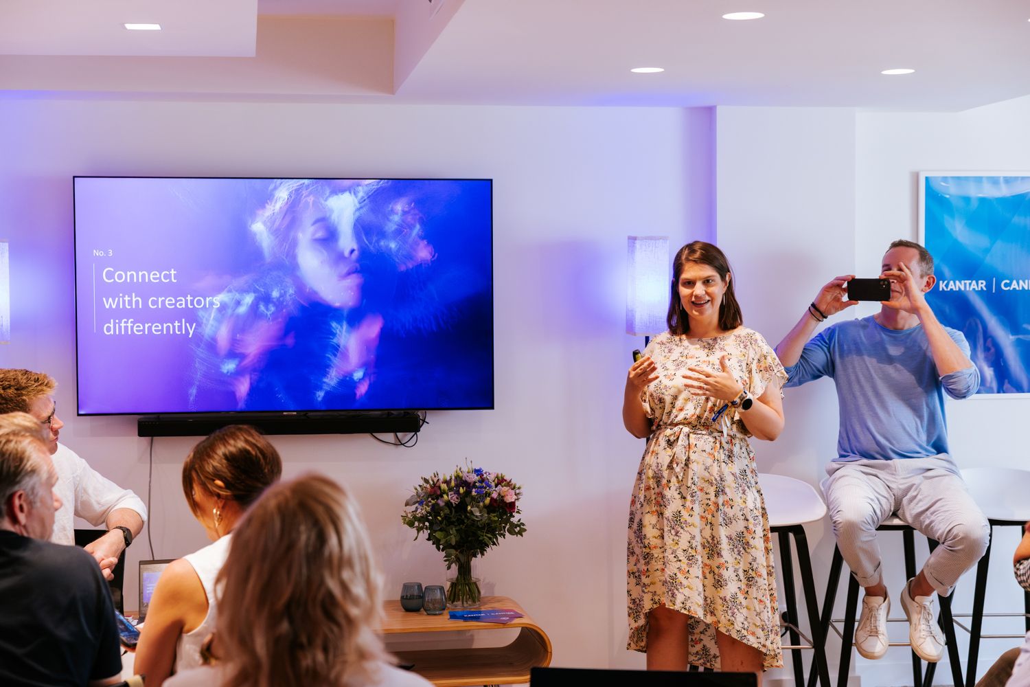 Modern office space with multiple presentation screens and purple ambient lighting during a business gathering.