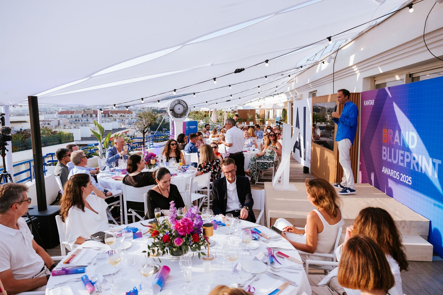 People enjoying food and drinks at an outdoor event under white tents with tables and decorative floral arrangements.