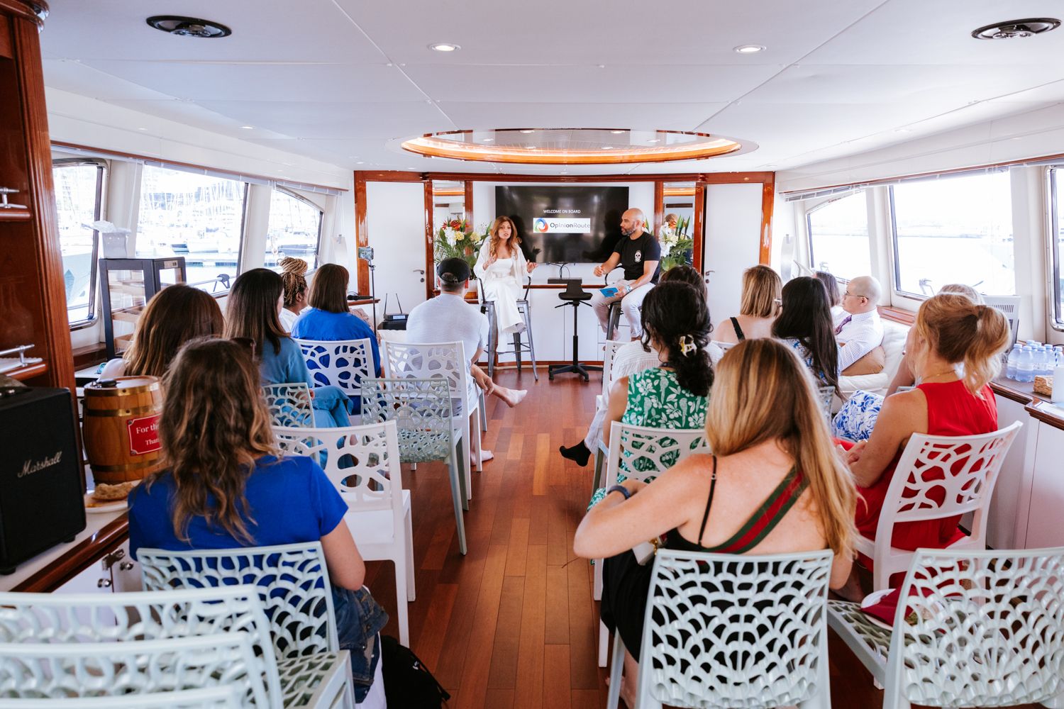 Passengers seated in white patterned chairs aboard a cruise ship deck during a scenic ocean voyage.