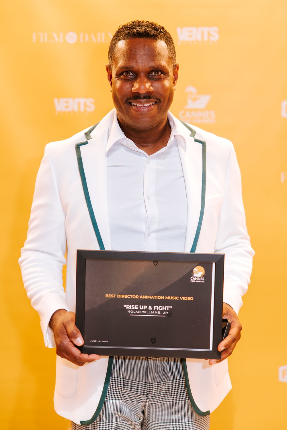 Chef in white jacket and green suspenders proudly displays award box against orange background.