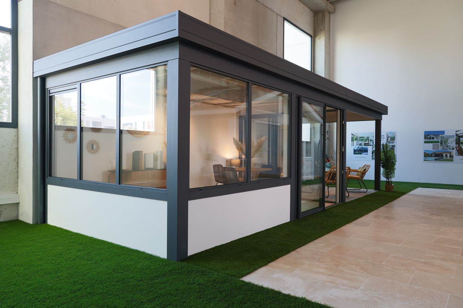 Contemporary glass veranda display with dark metal frame and artificial turf in indoor showroom.