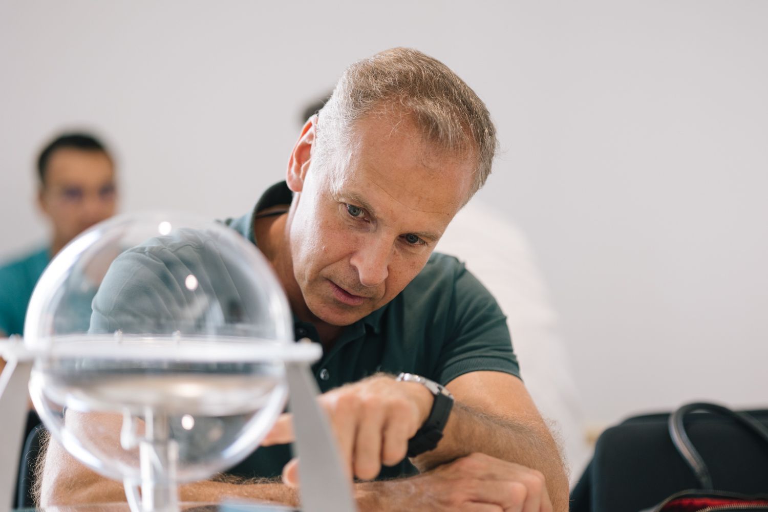 Someone examining a clear glass sphere or scientific instrument on a table.