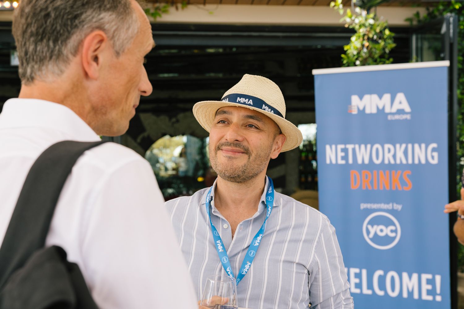 Networking event participants conversing near MMA welcome banner outdoors.