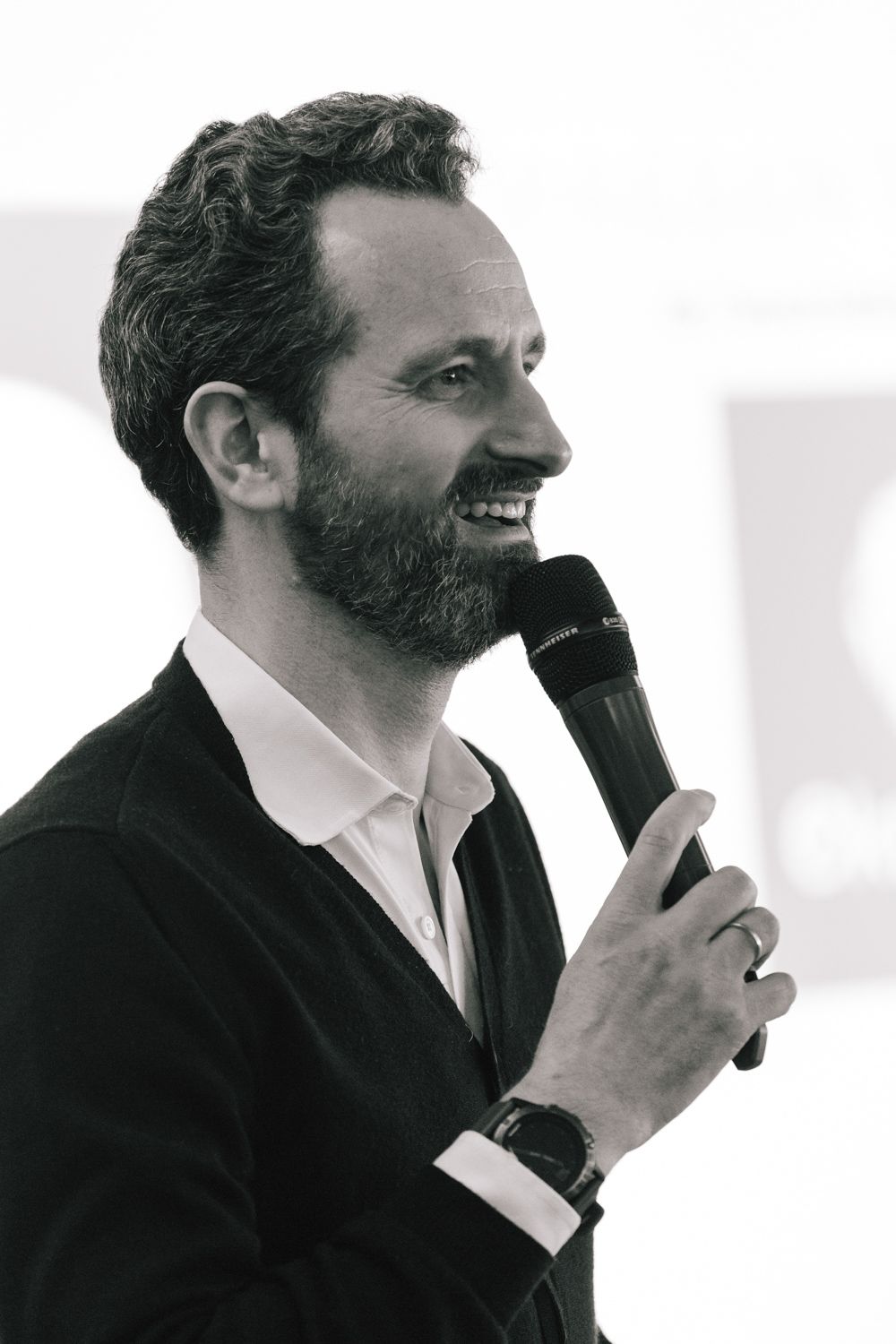 Black and white image of a speaker holding a microphone and smiling during a presentation.