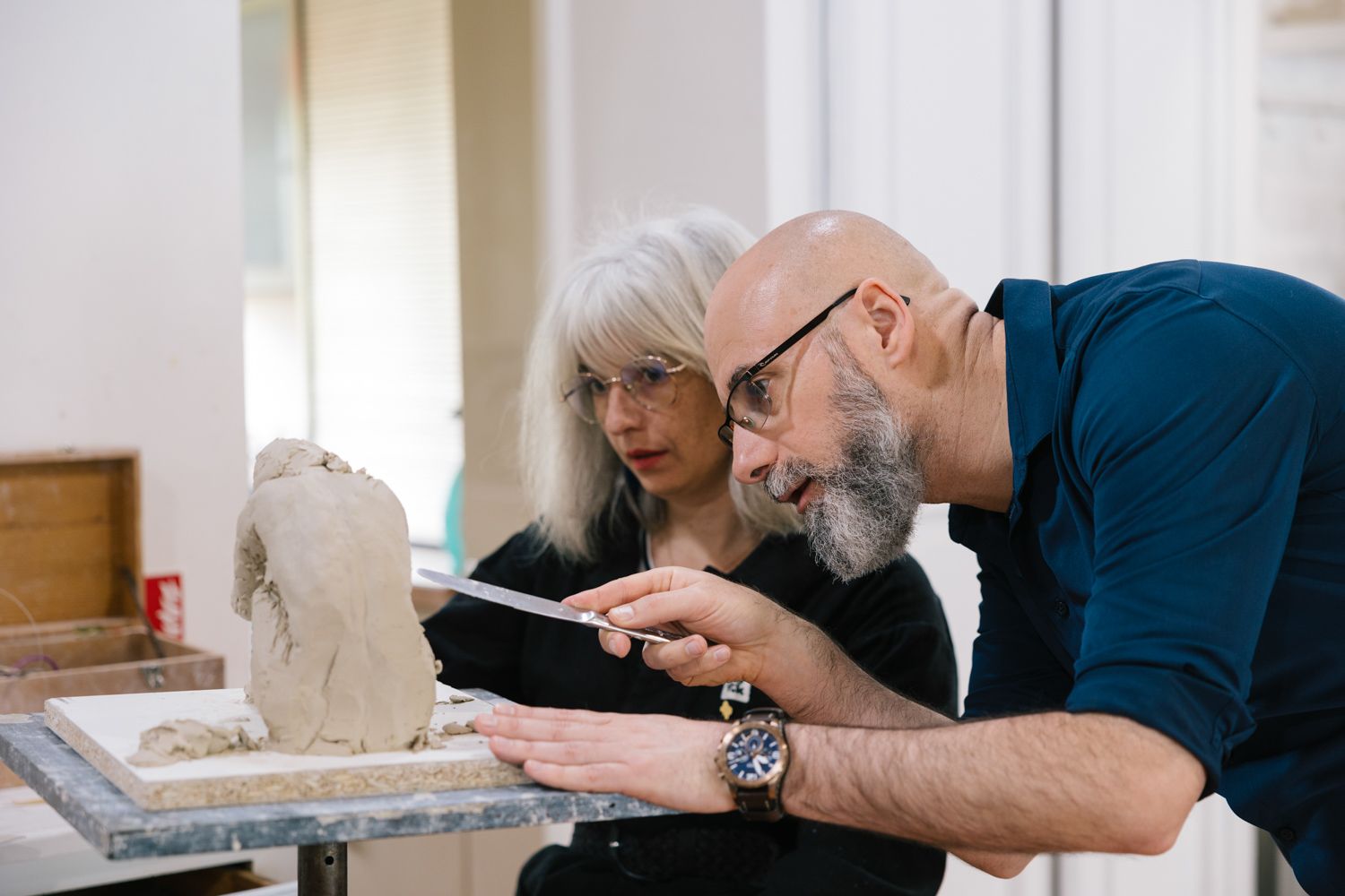 Two people examining a small sculpture or bust in an art studio setting.