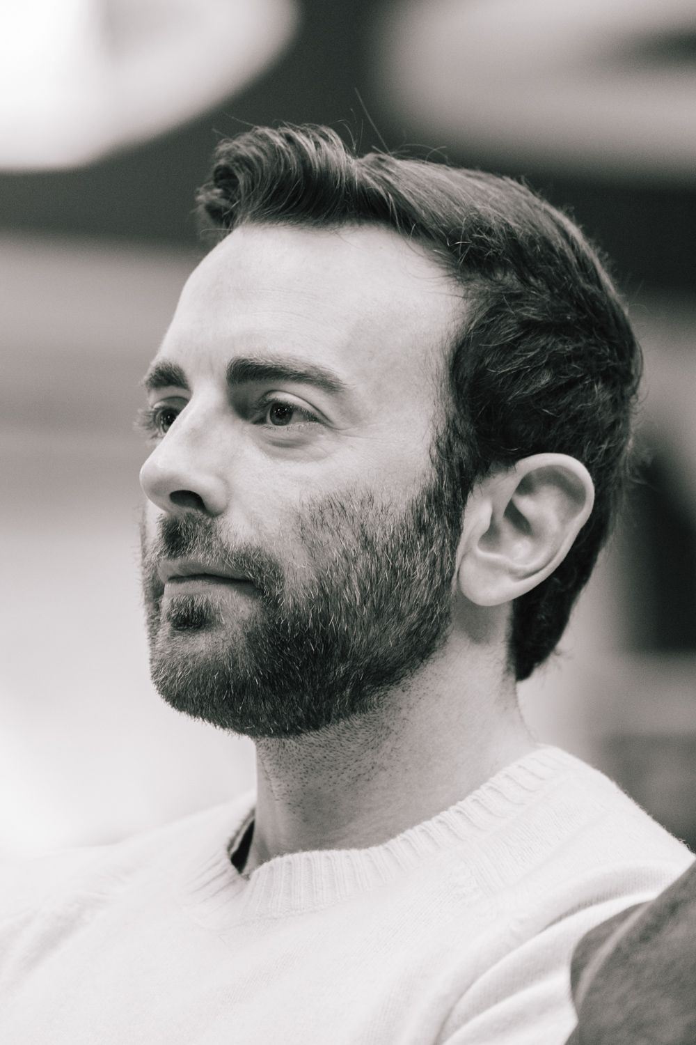 Black and white portrait of a person with a beard wearing a white shirt and contemplative expression.