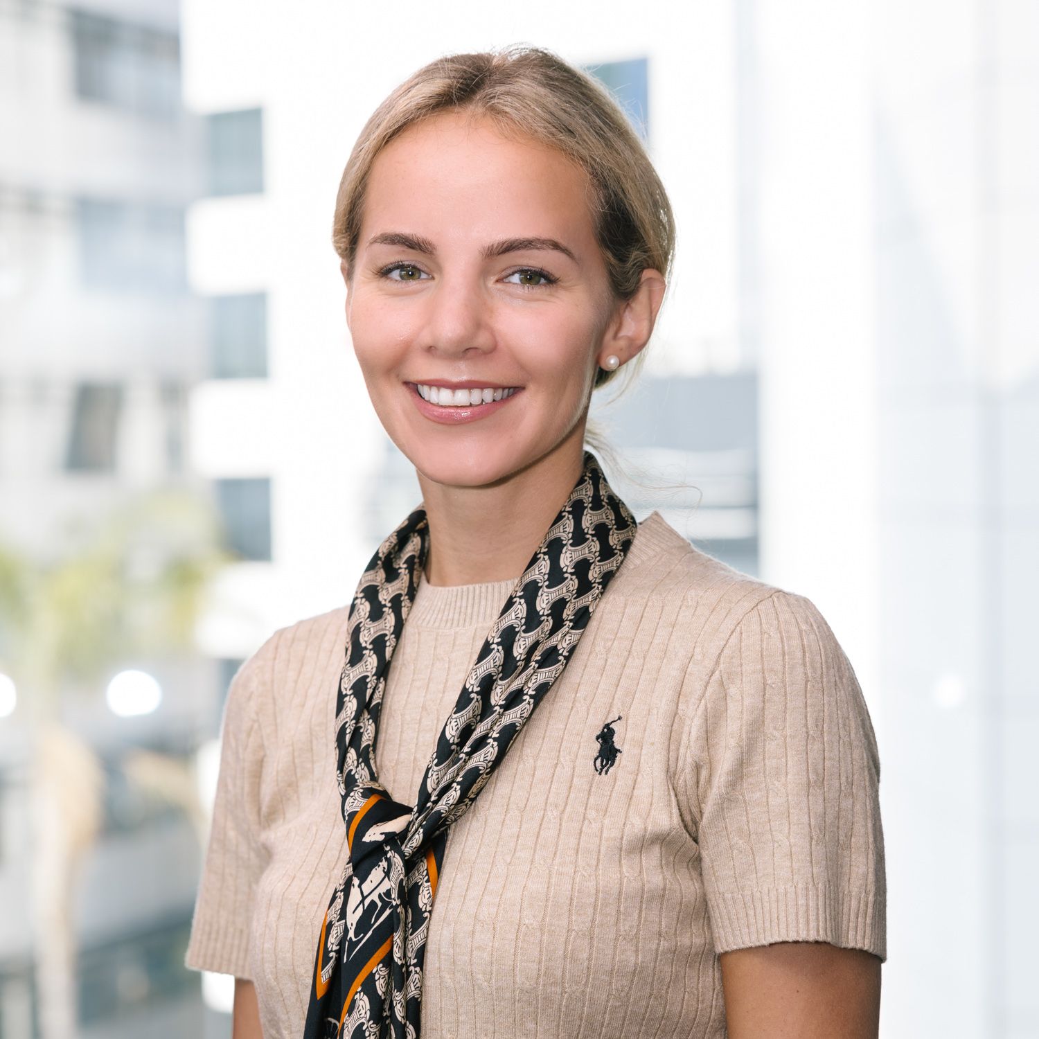 Professional wearing beige sweater and patterned scarf in corporate setting.