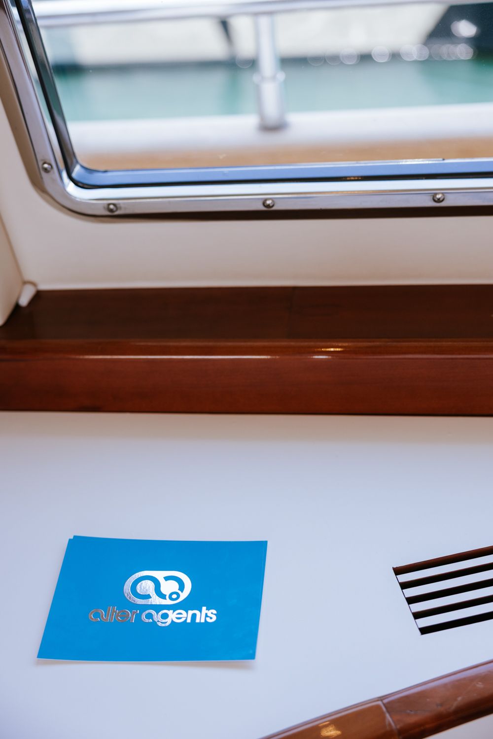 Modern boat interior detail showing sleek brown wood paneling and window frame against a light background.
