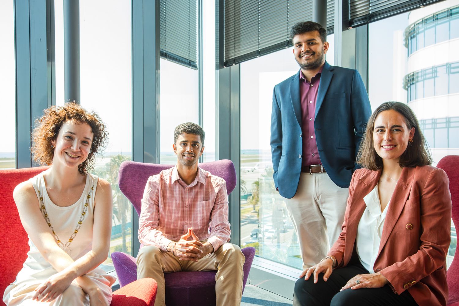 Group of professionals sitting and standing in a modern office lounge with city views.