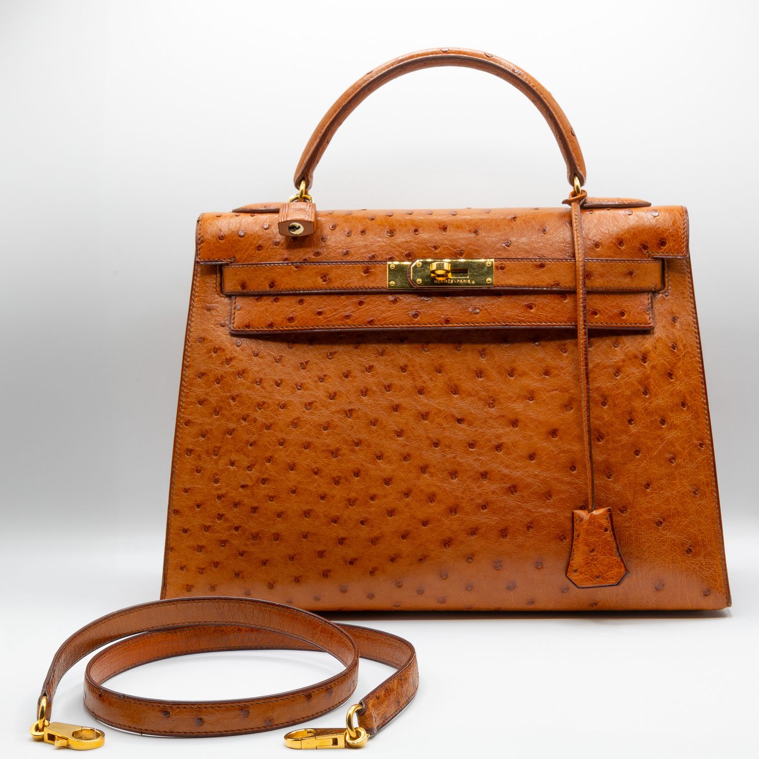 Luxury tan ostrich leather handbag with shoulder strap against white background.