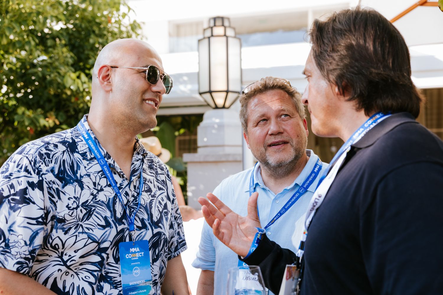 A group of people having an animated conversation while sitting at an outdoor table during a sunny day.