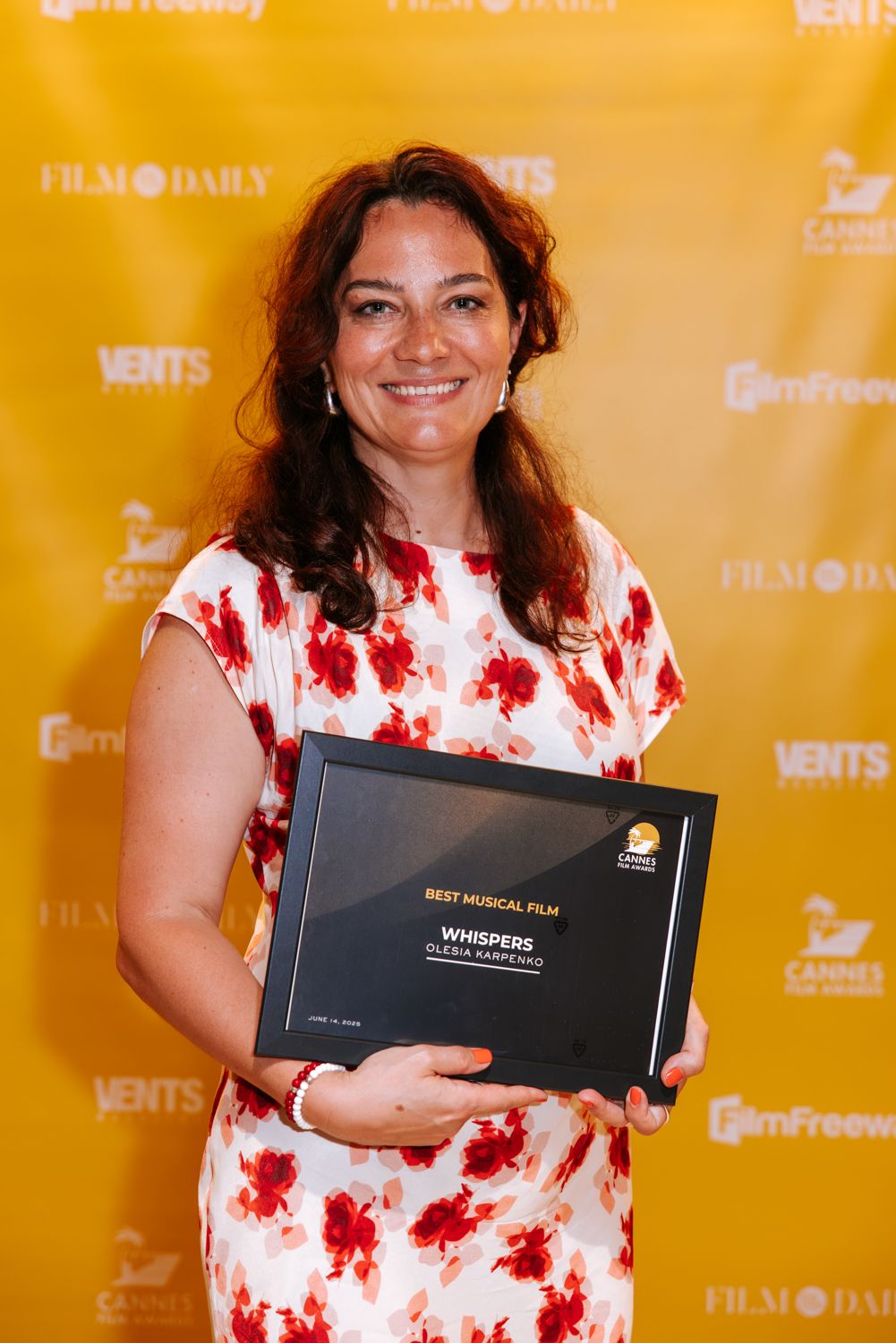 Award winner holds black trophy box against yellow backdrop at film festival ceremony.