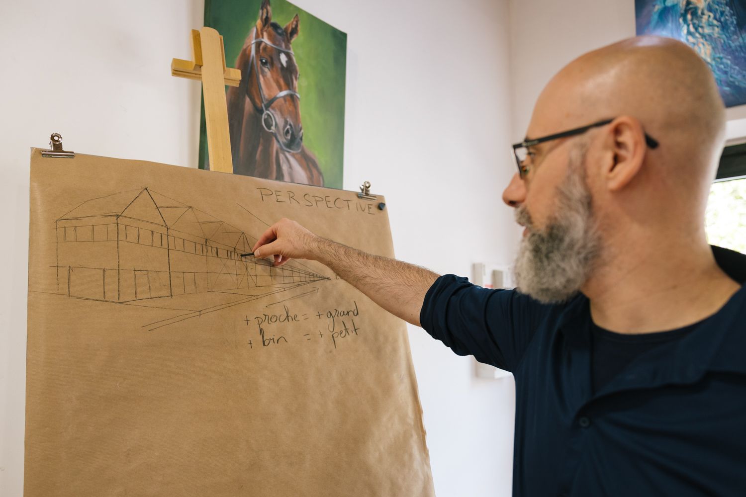 An artist sketches architectural drawings on brown paper in an art-filled studio space.