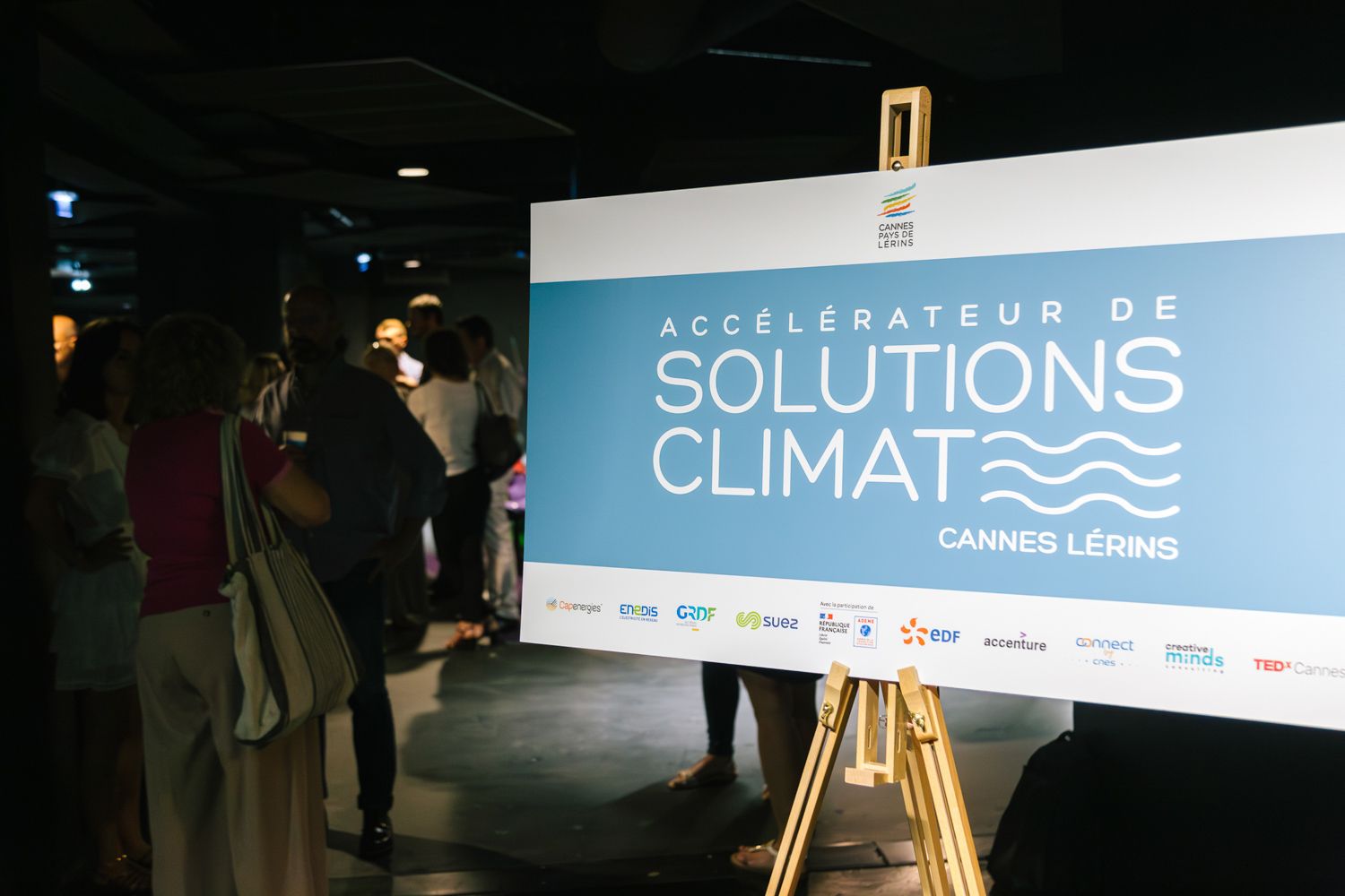 Climate solutions event banner displayed on easel with attendees in background.