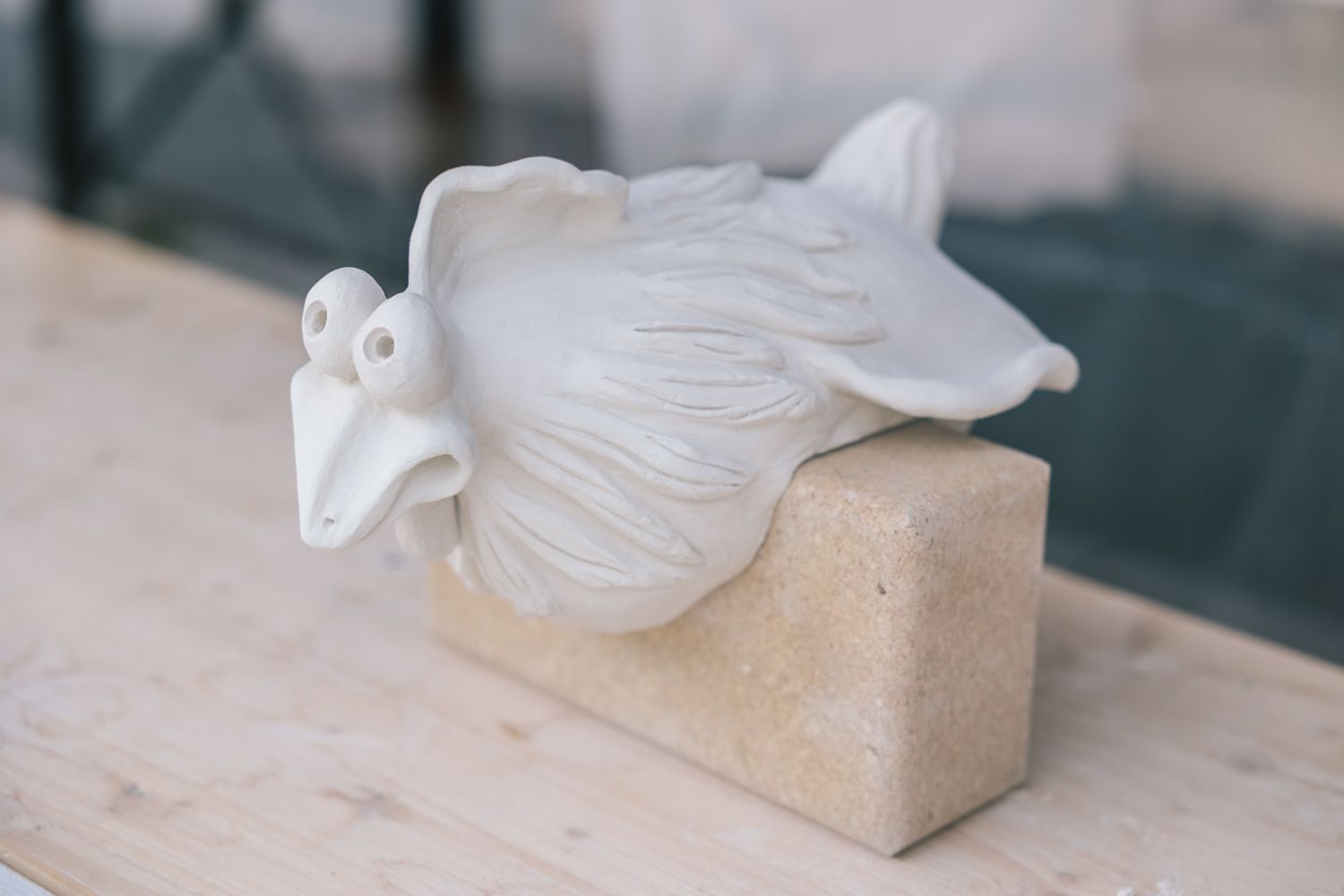 White ceramic bird sculpture resting on a stone block.