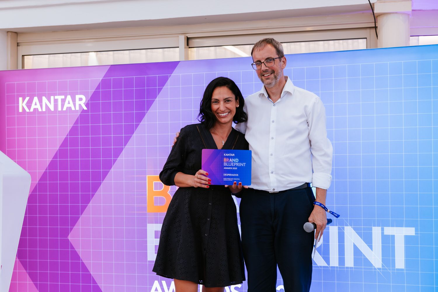 People receiving awards at a business event with blue and pink stage lighting and Kantar branding visible.