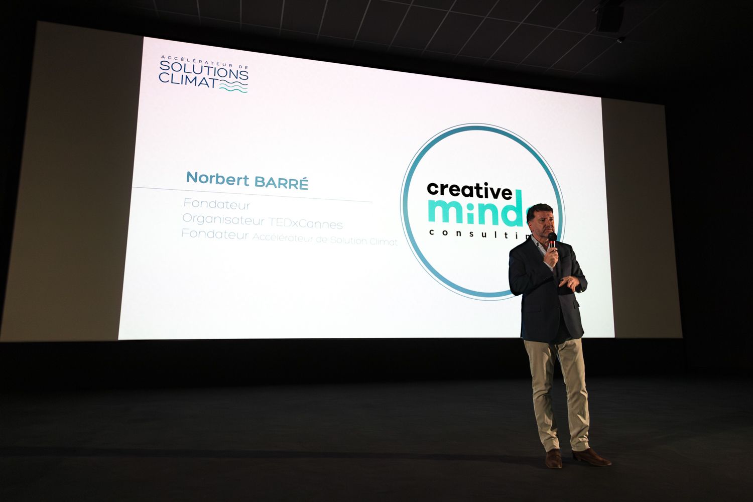 Presenter speaking on stage with Creative Mind Consult presentation slide displayed.