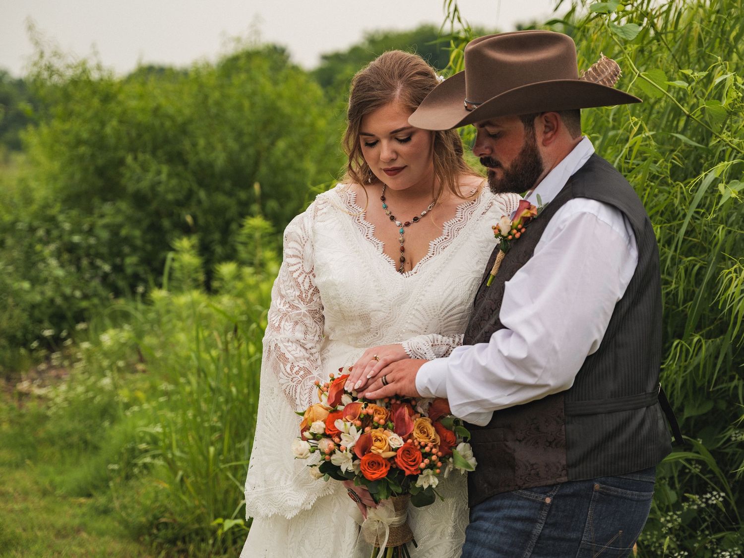 A couple shares a romantic moment in white wedding attire surrounded by lush green outdoor scenery.
