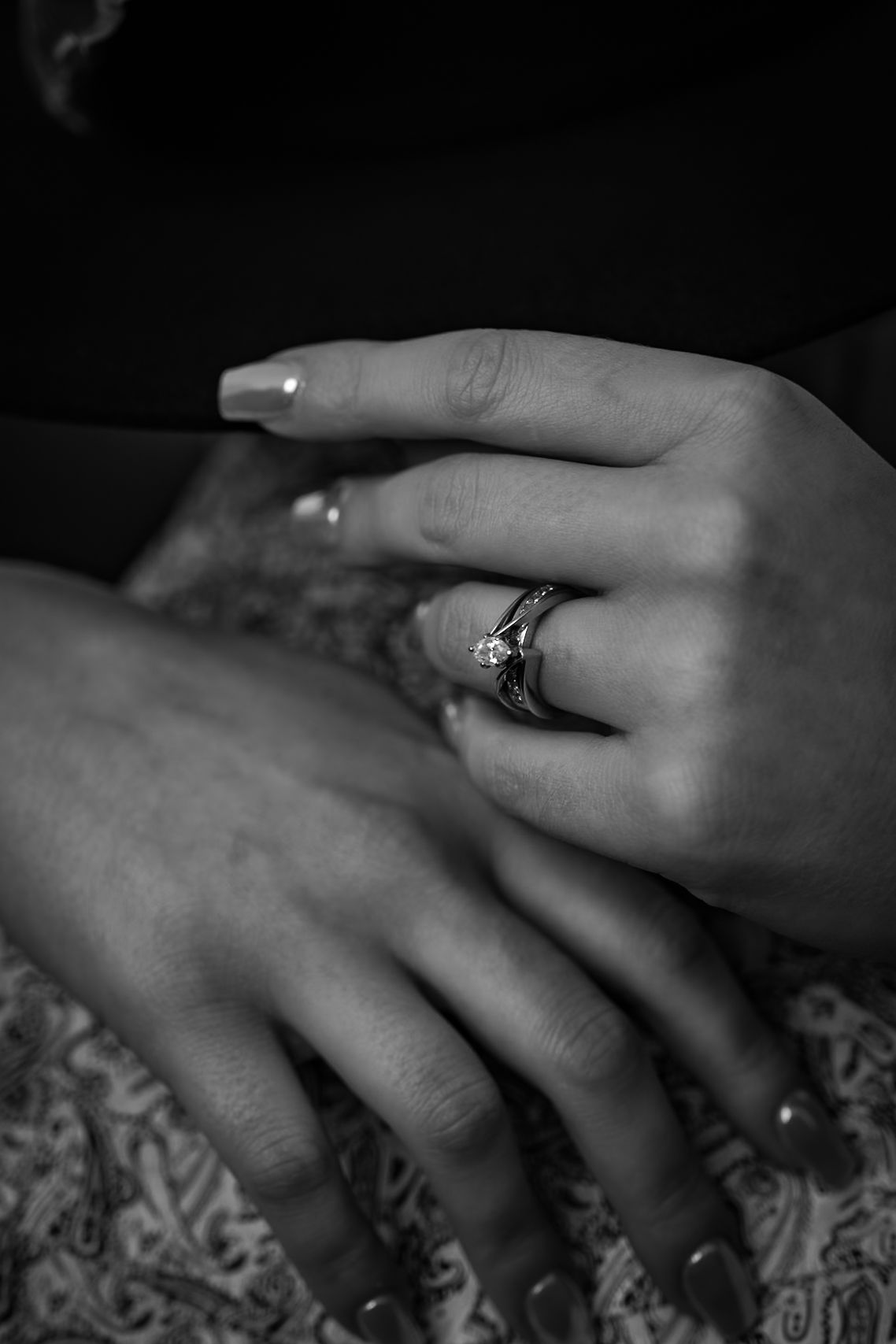 Black and white detail shot of hands with an engagement ring against textured fabric.
