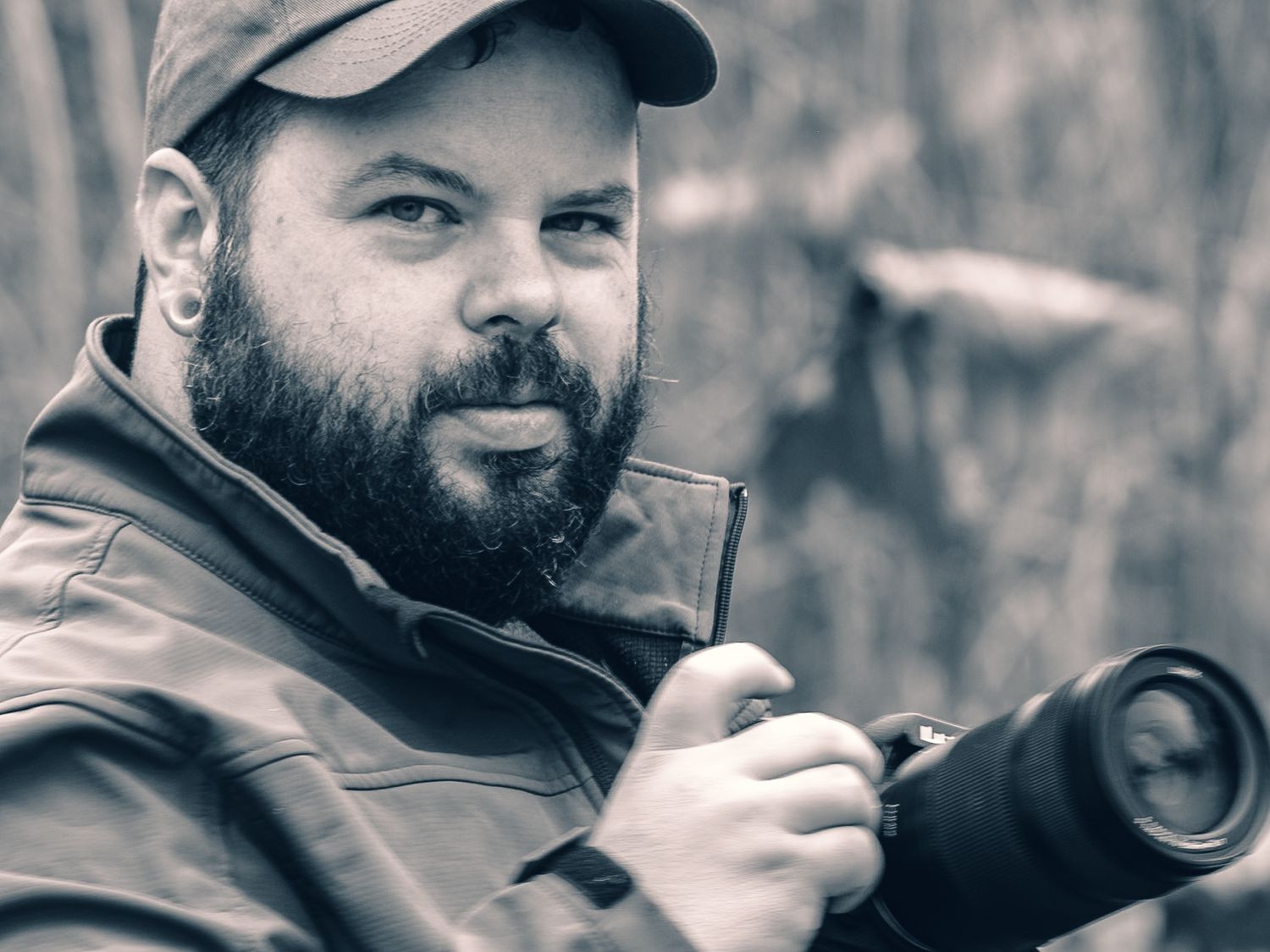Wildlife photographer with beard wearing baseball cap and using telephoto lens.