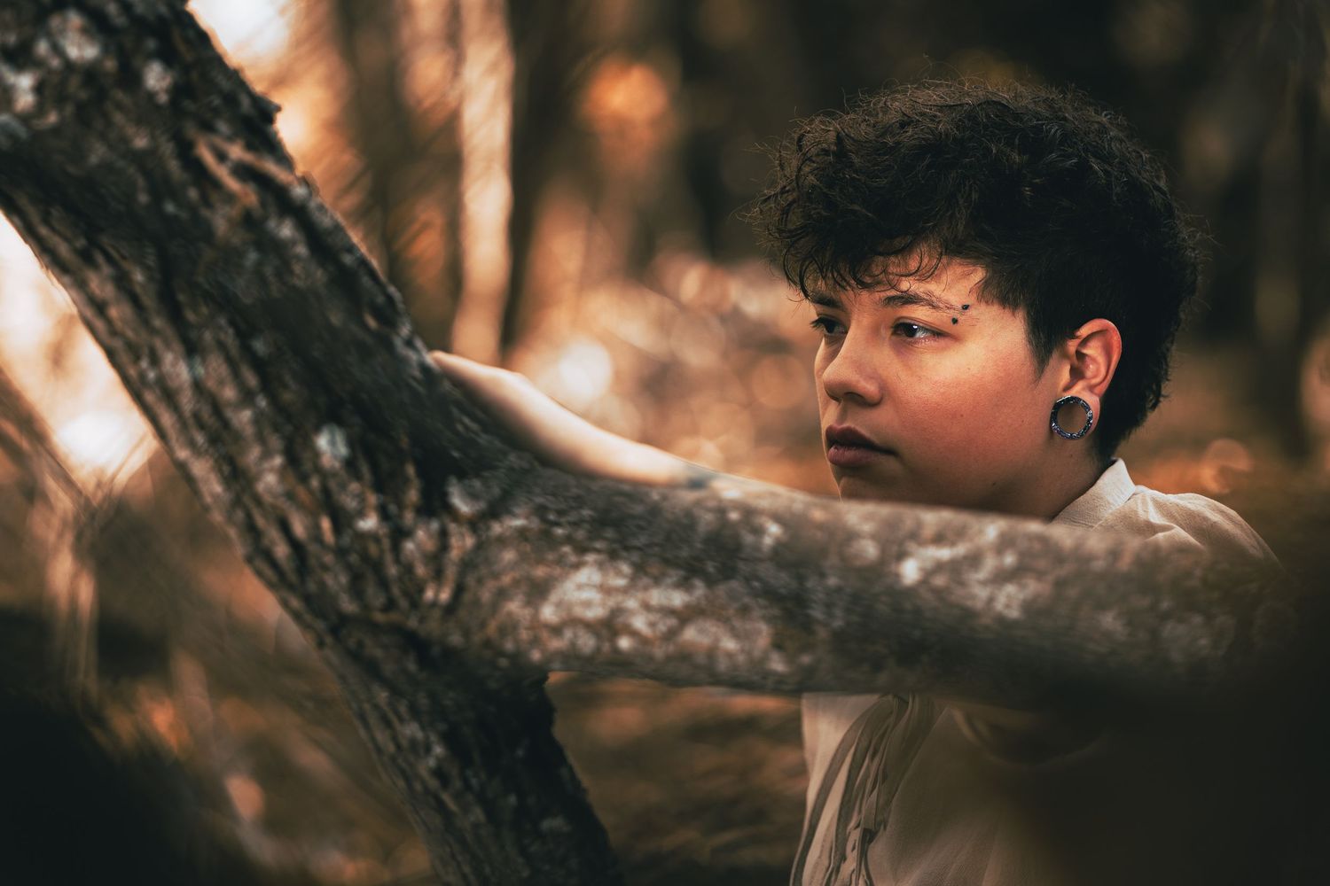 A dreamy forest portrait shot through tree branches with warm autumn lighting.
