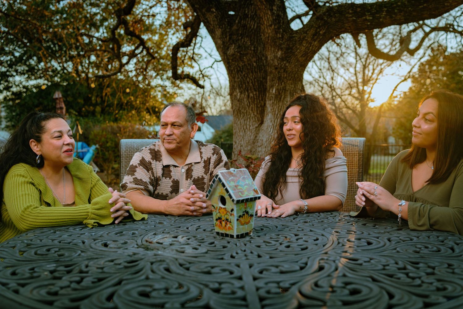 Friends gather around an ornate patio table during sunset for drinks and conversation.
