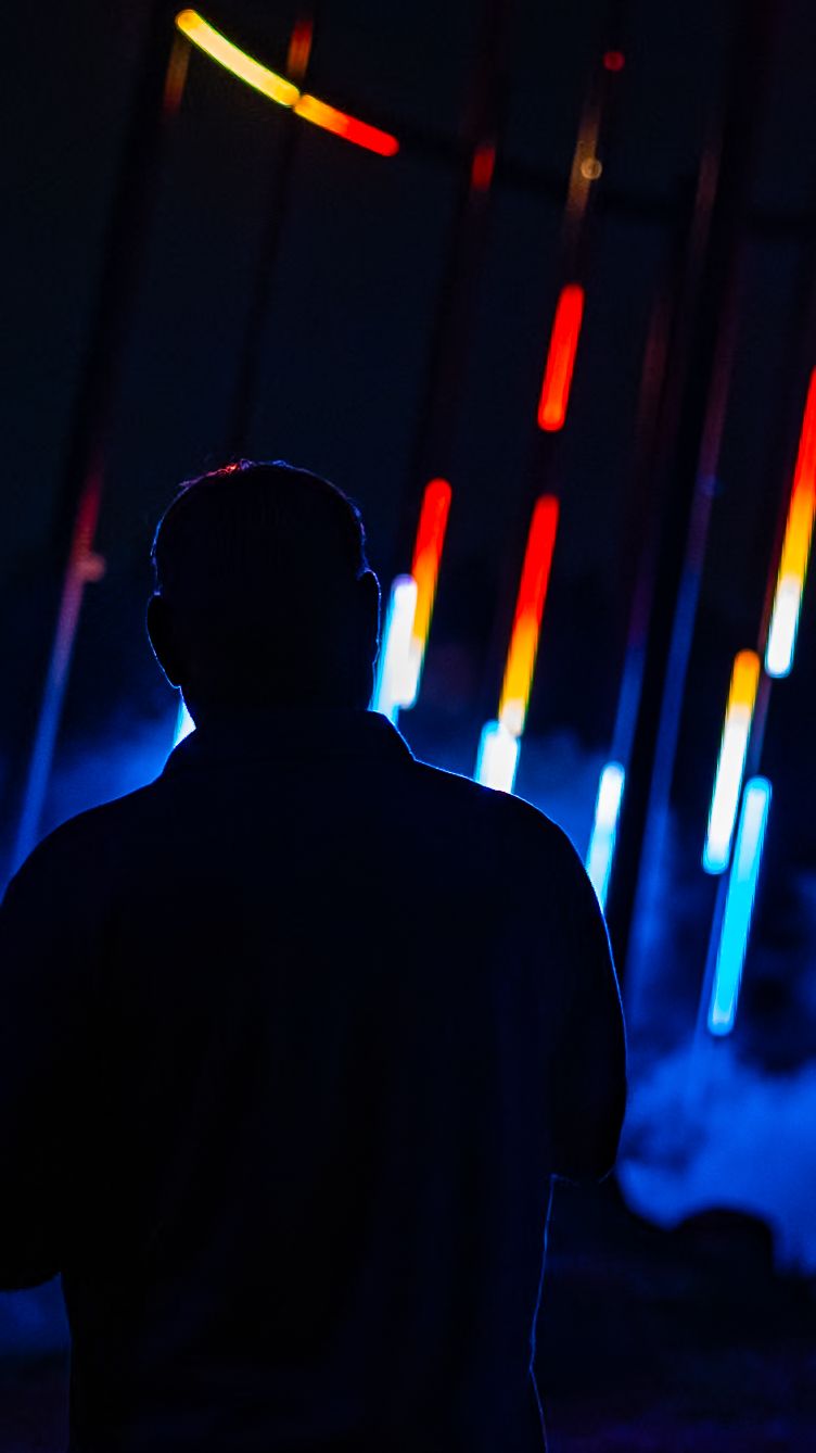Silhouette against colorful neon lights in dark atmospheric setting.