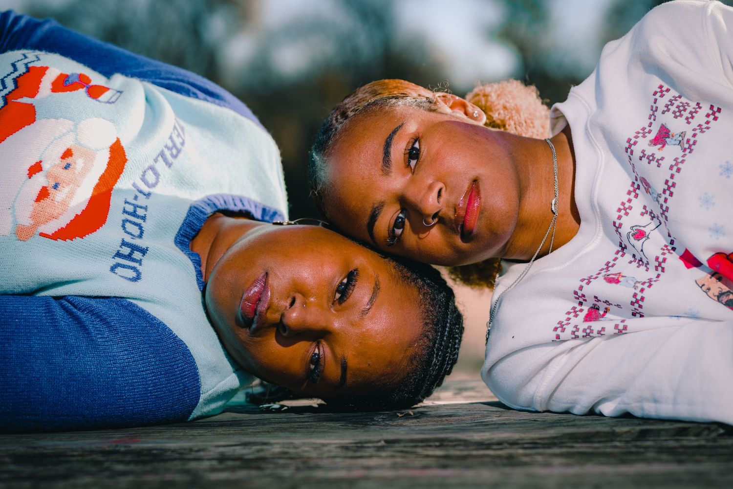 Two people in holiday sweaters lying close together on wooden surface.