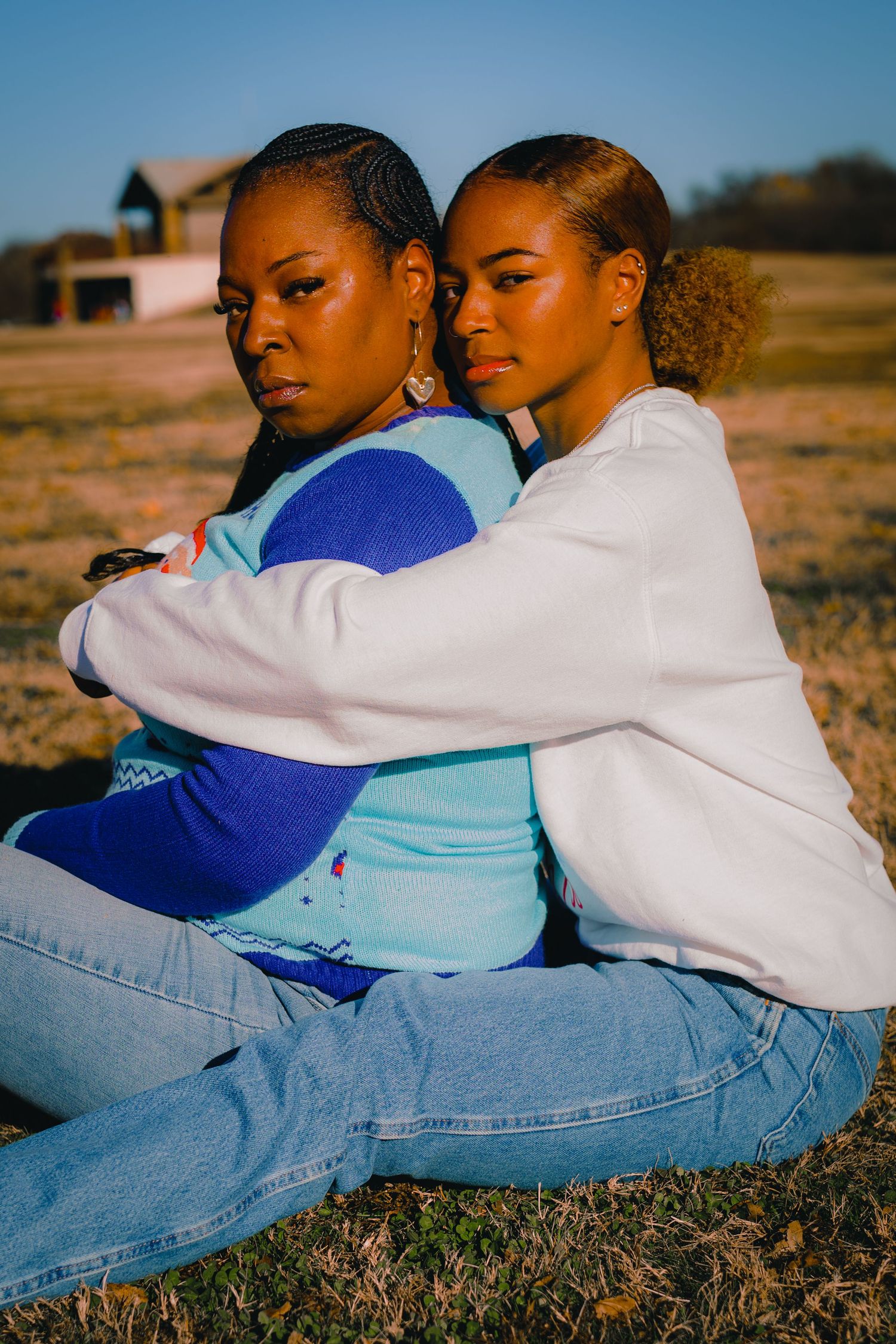 Two people in casual clothing sitting back-to-back on grass during sunset.