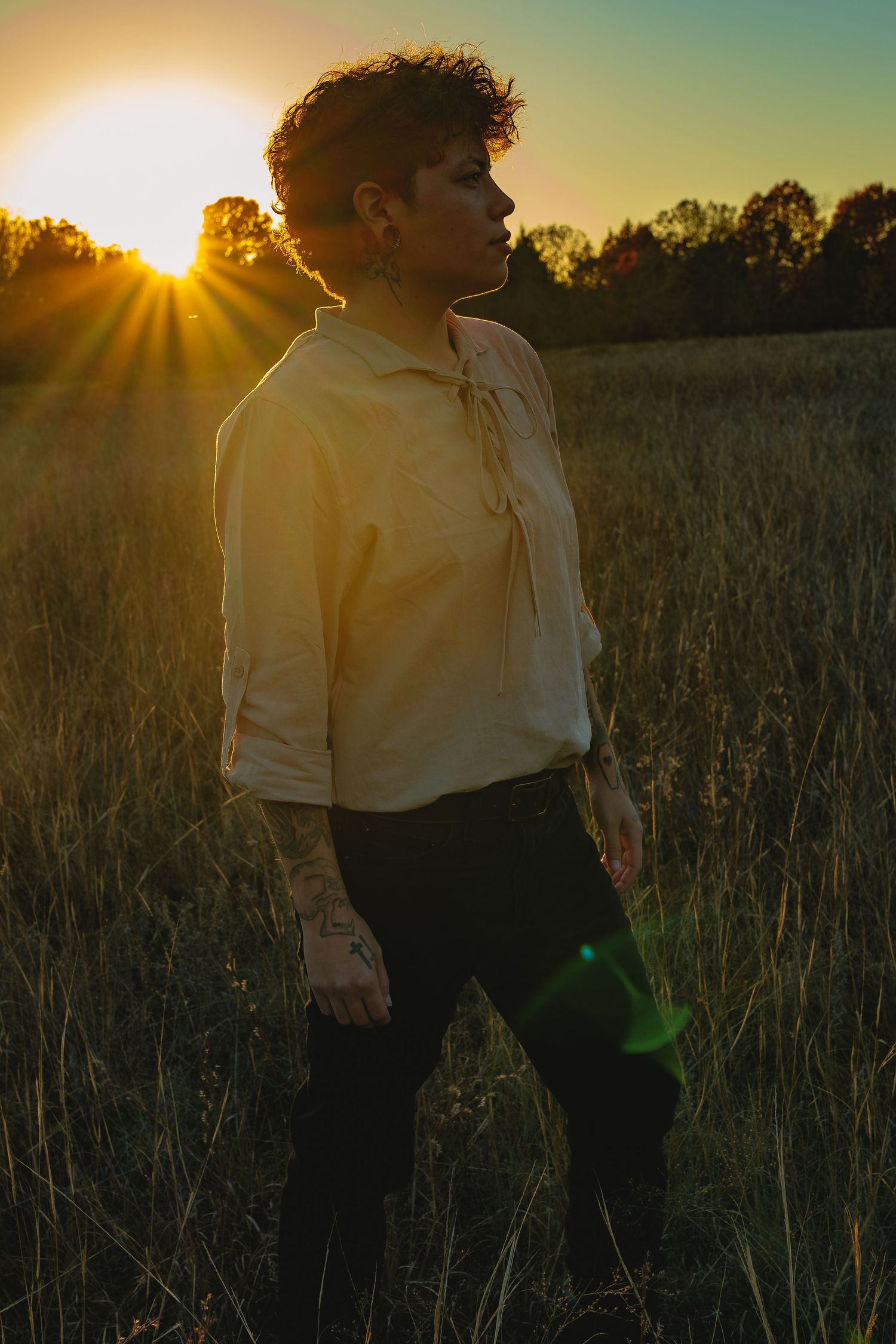 A silhouetted figure in white shirt standing in golden sunlit field at sunset.