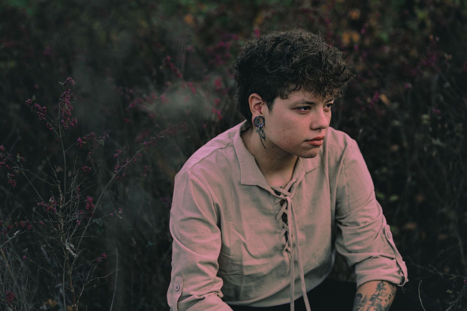 Someone in a beige button-up shirt sits outdoors against a dark natural background on an autumn day.
