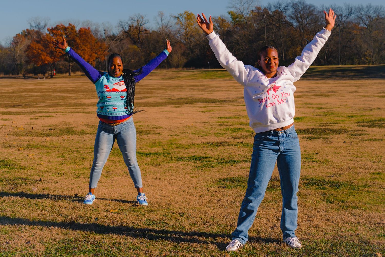 Two people with arms raised celebrating in an open field during autumn.