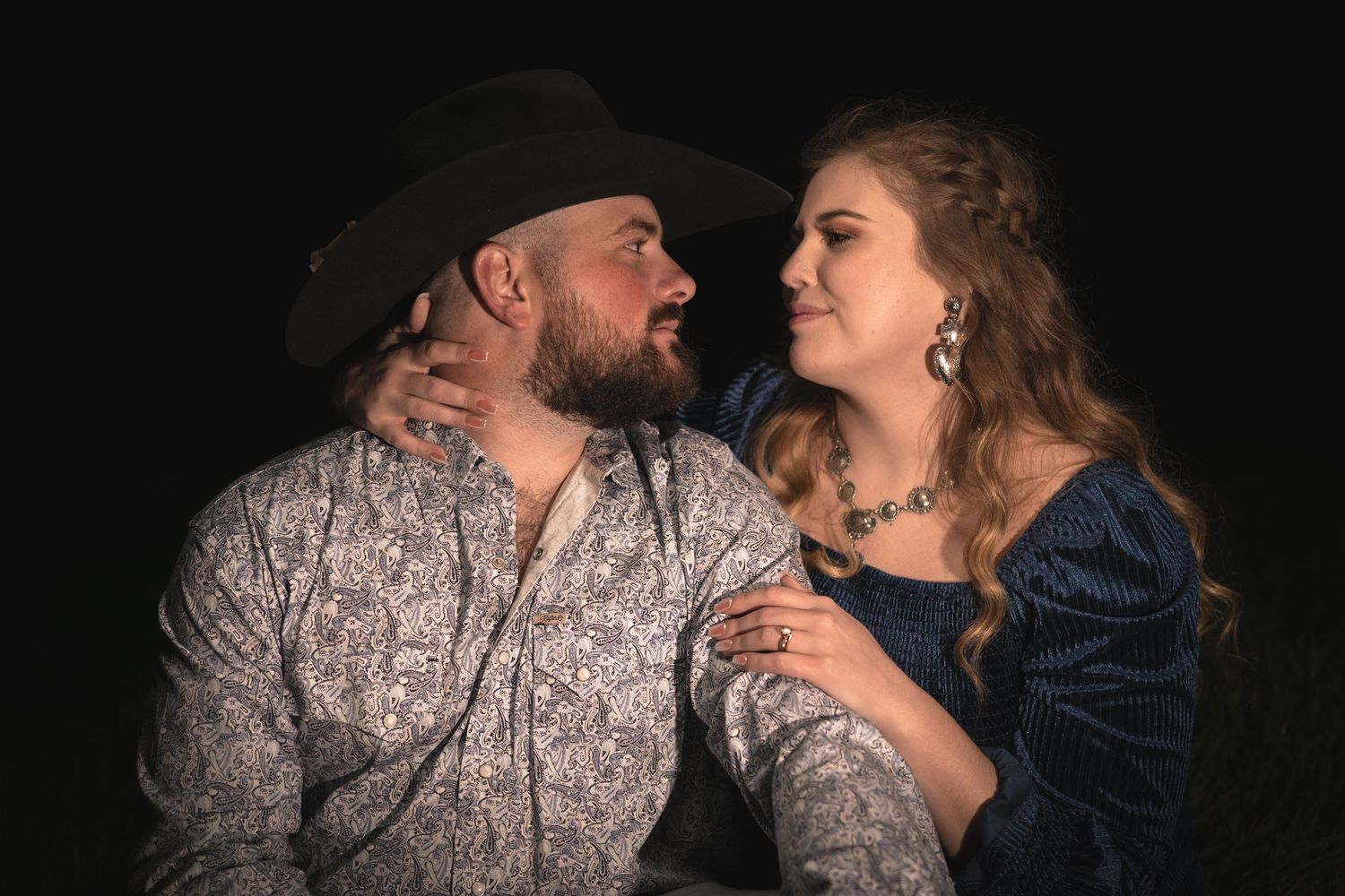 Couple in western attire sharing intimate moment against dark background.