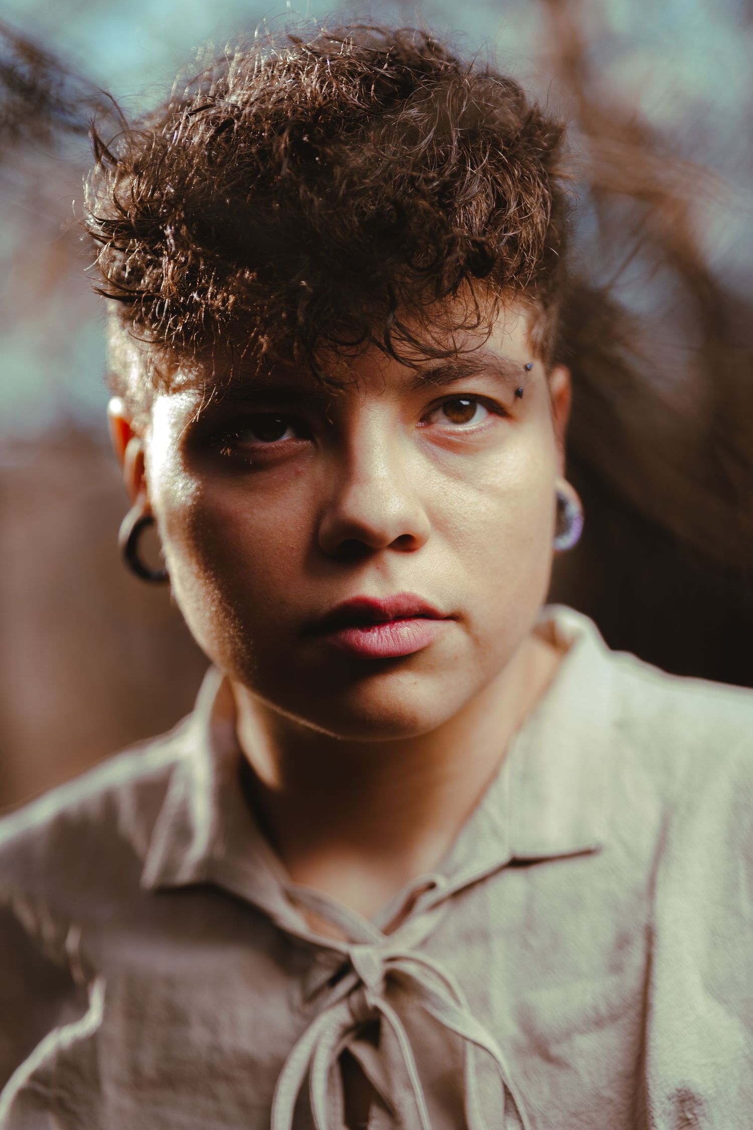Close-up portrait with curly hair and brown jacket in soft natural lighting.