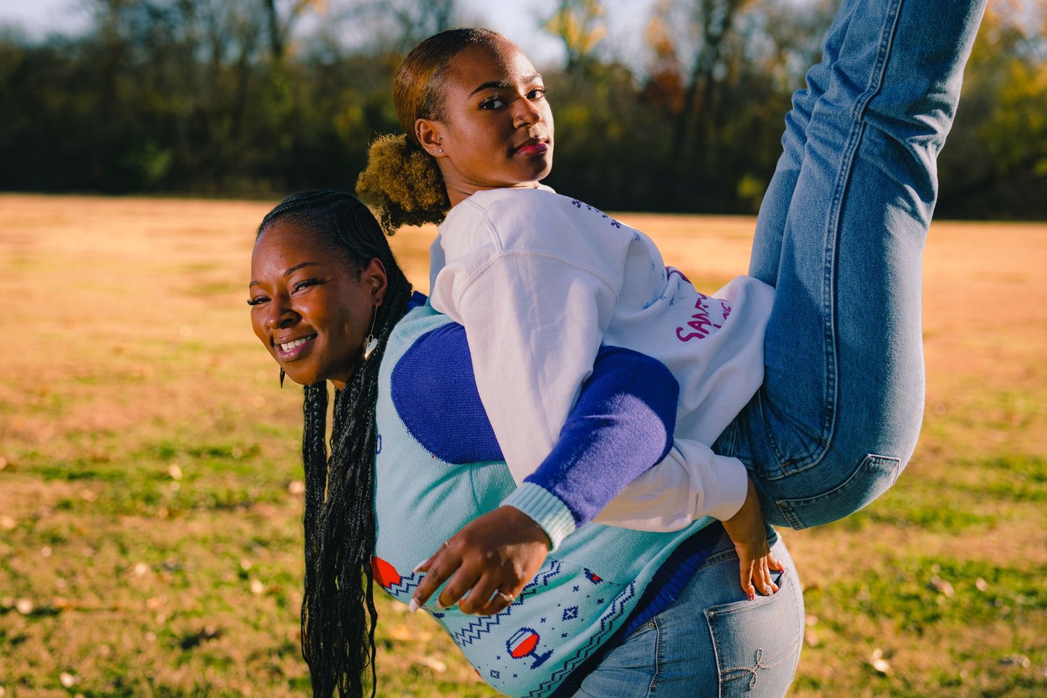 Two people in casual outfits playfully pose together in an outdoor field setting.